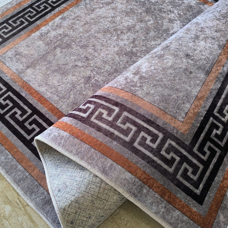 Un tapis gris chiné avec un motif de méandres géométriques gris foncé et des bordures orange et grises, partiellement enroulé