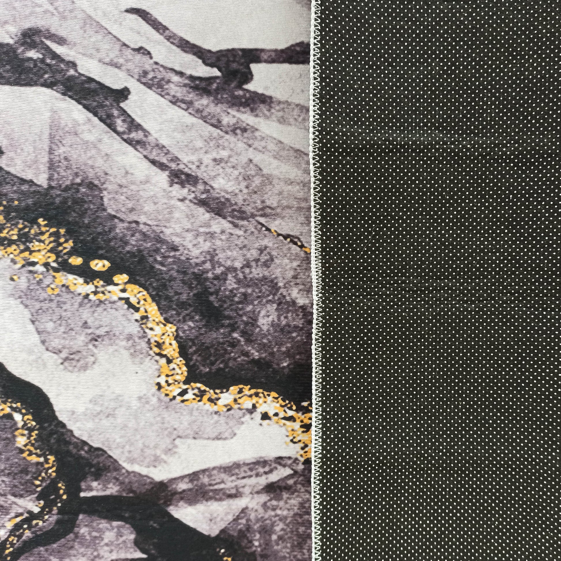 Tapis au motif abstrait gris, noir et doré, avec un verso antidérapant noir à pois blancs et une couture visible