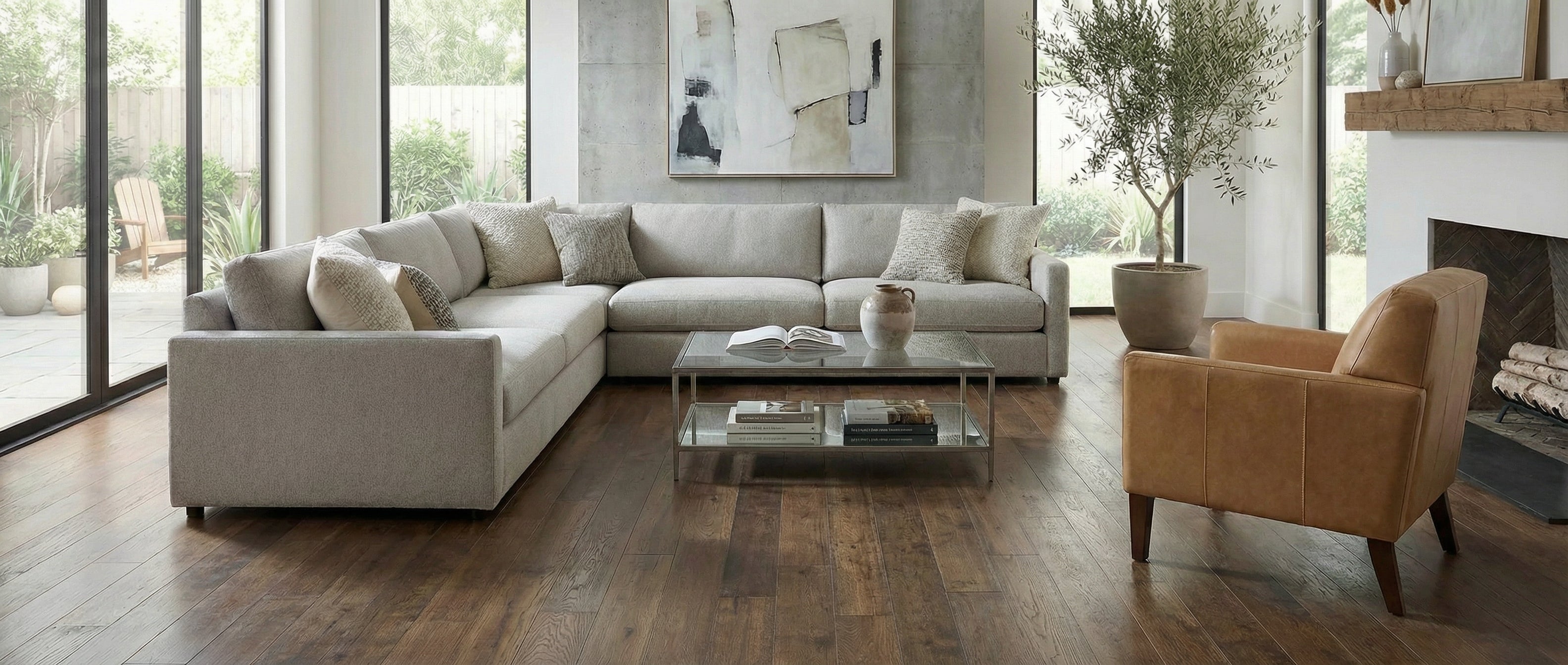 Pièce lumineuse, canapé clair, fauteuil cuir marron, sol bois foncé, tableau abstrait. Espace vide pour un tapis