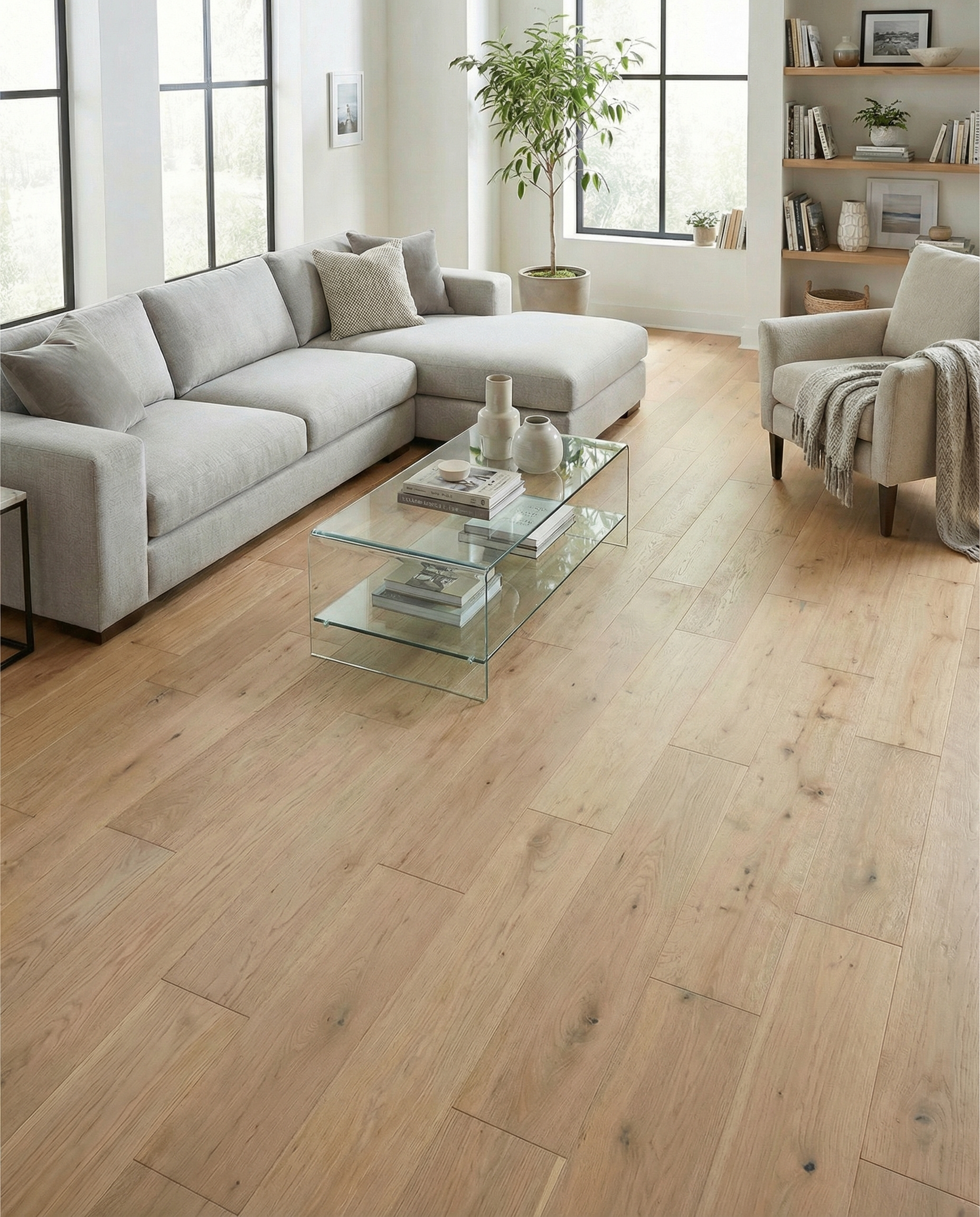 Pièce lumineuse avec plancher en bois clair, canapé gris, table basse en verre, fauteuil et bibliothèque, ambiance