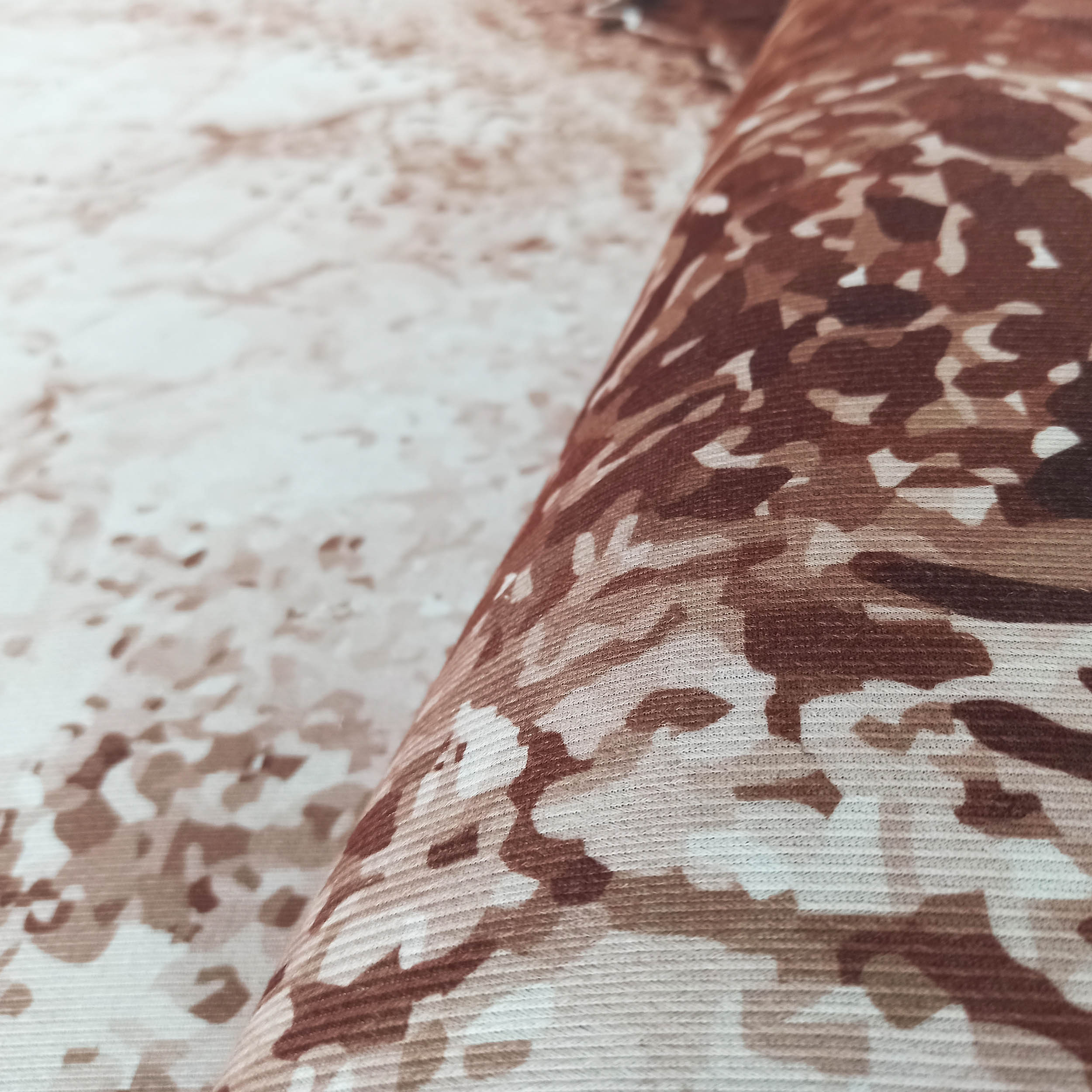 Gros plan sur un tapis texturé aux motifs abstraits et irréguliers dans des tons de marron, beige et crème, partiellement roulé
