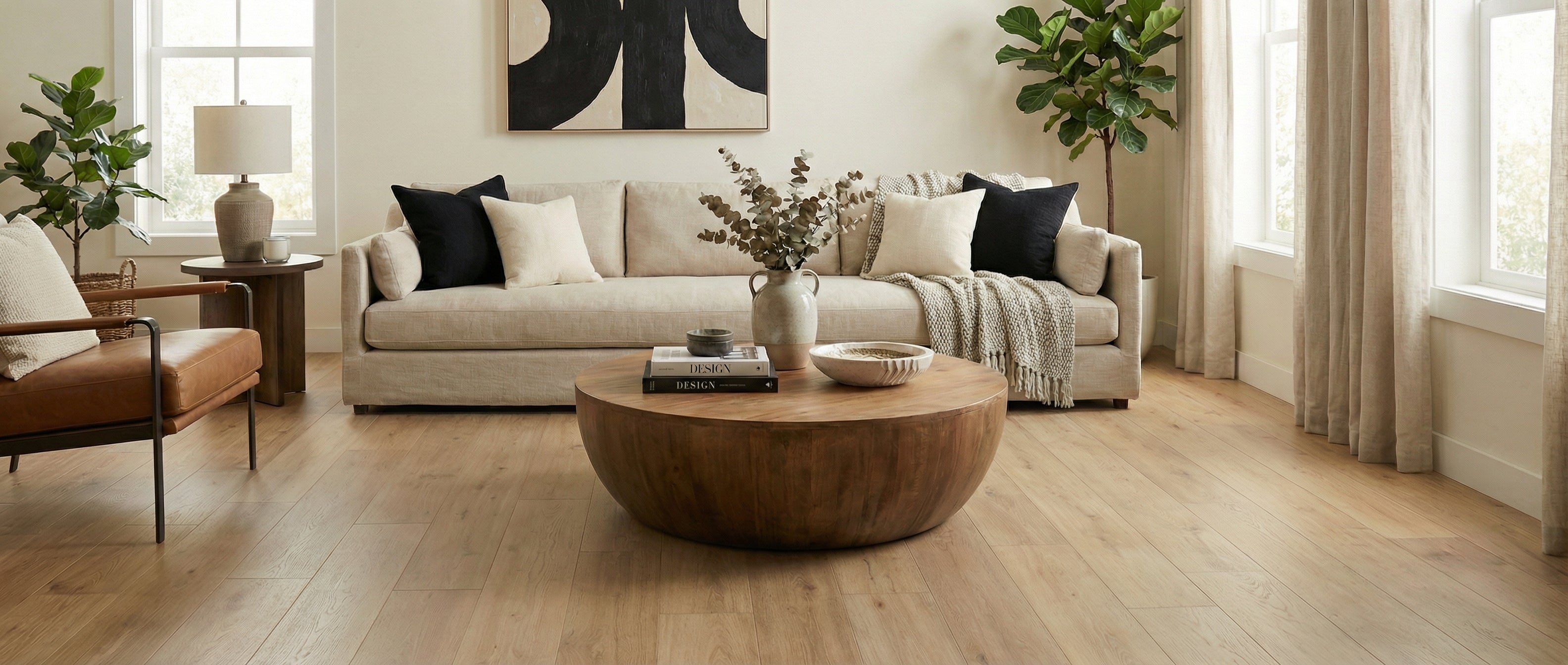 Pièce lumineuse, ambiance neutre. Sol clair, canapé beige, coussins noirs. Table basse ronde en bois. Potentiel déco