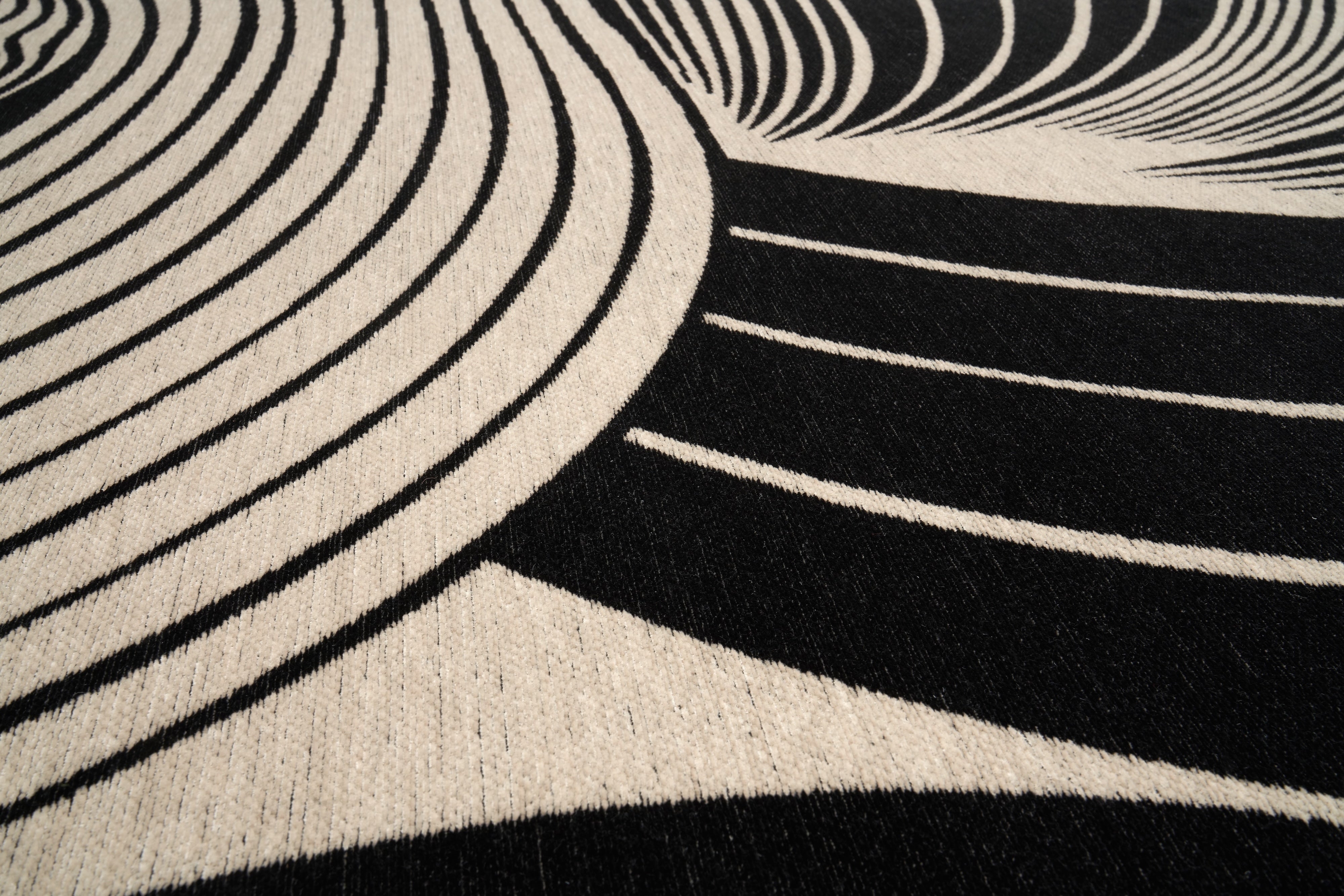 Gros plan sur un tapis moderne noir et beige Mistral, révélant la texture et les fibres du tissu avec des motifs géométriques courbes.