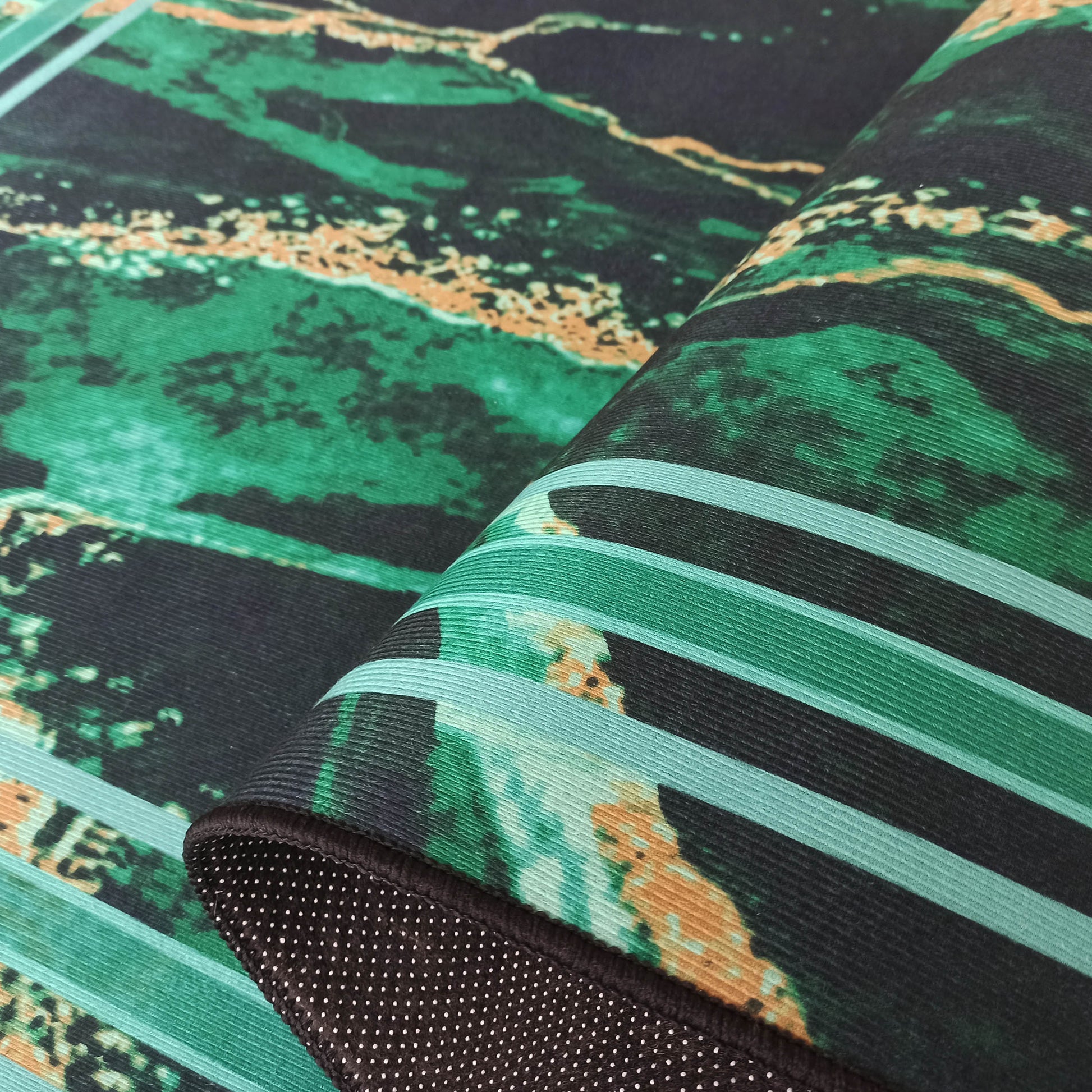 Tapis aux motifs marbrés vert foncé, émeraude et ocre, plié pour révéler des bandes vertes et un envers antidérapant noir à pois blancs