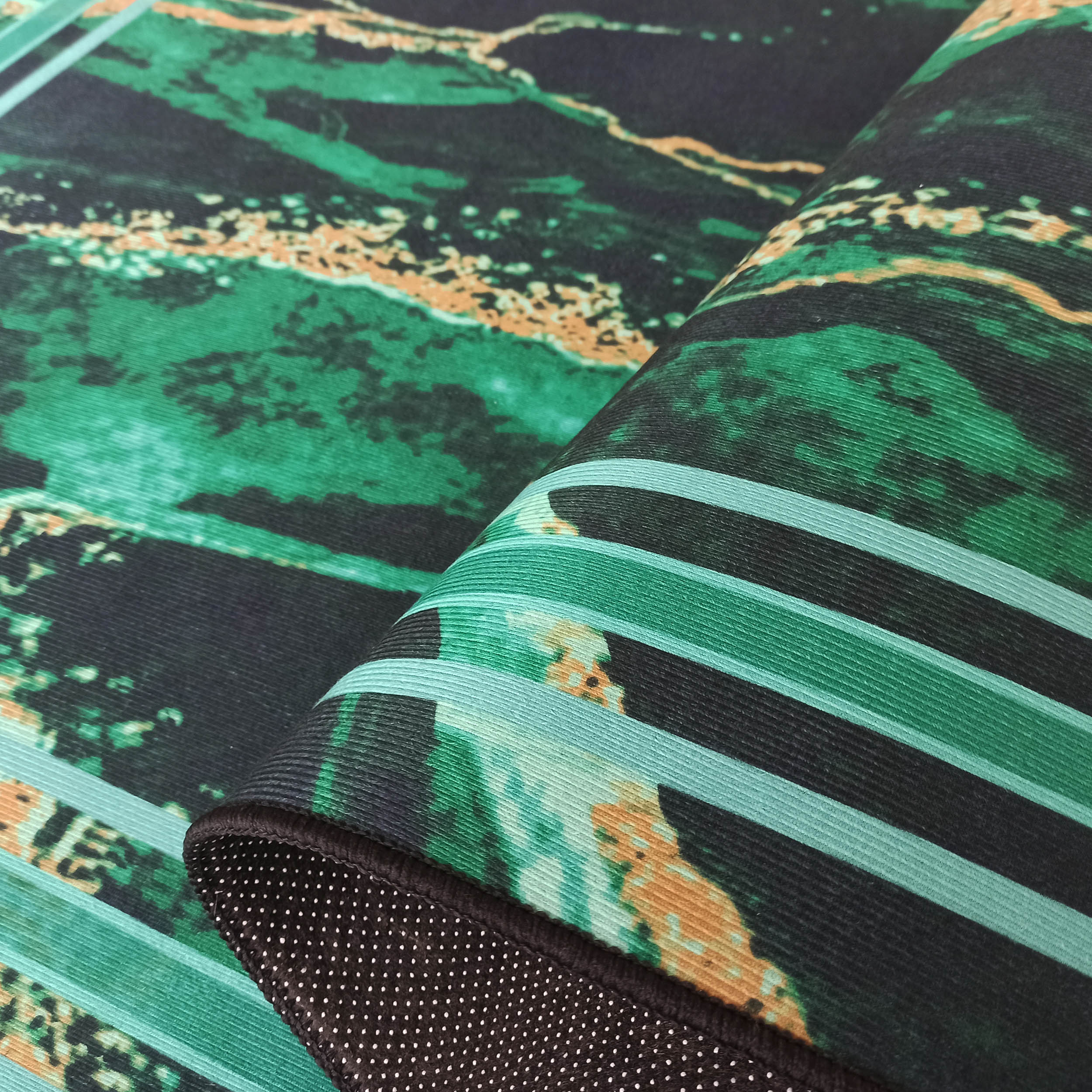 Tapis aux motifs marbrés vert foncé, émeraude et ocre, plié pour révéler des bandes vertes et un envers antidérapant noir à pois blancs