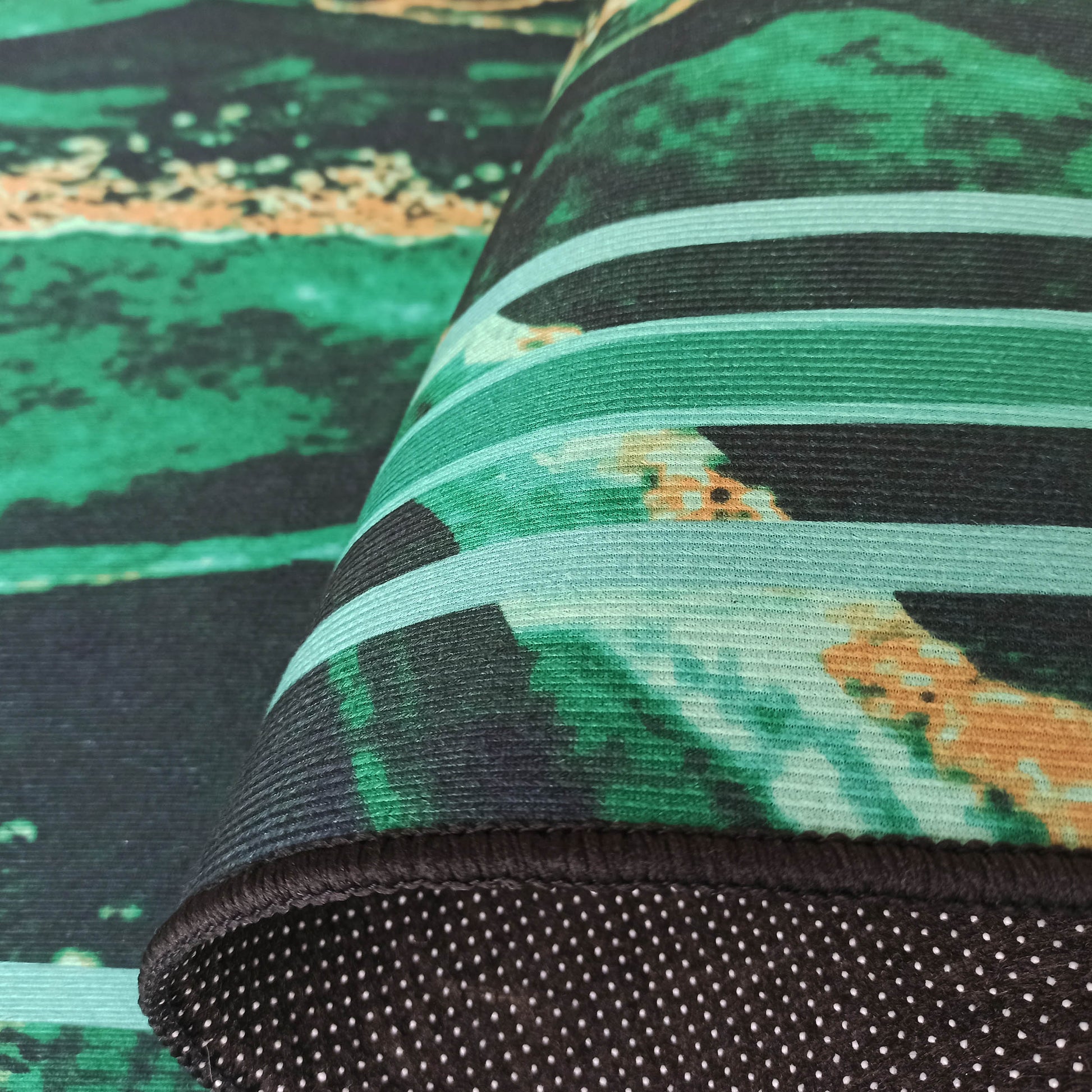 Tapis partiellement roulé aux motifs abstraits verts, noirs et orangés, révélant un envers noir à pois blancs