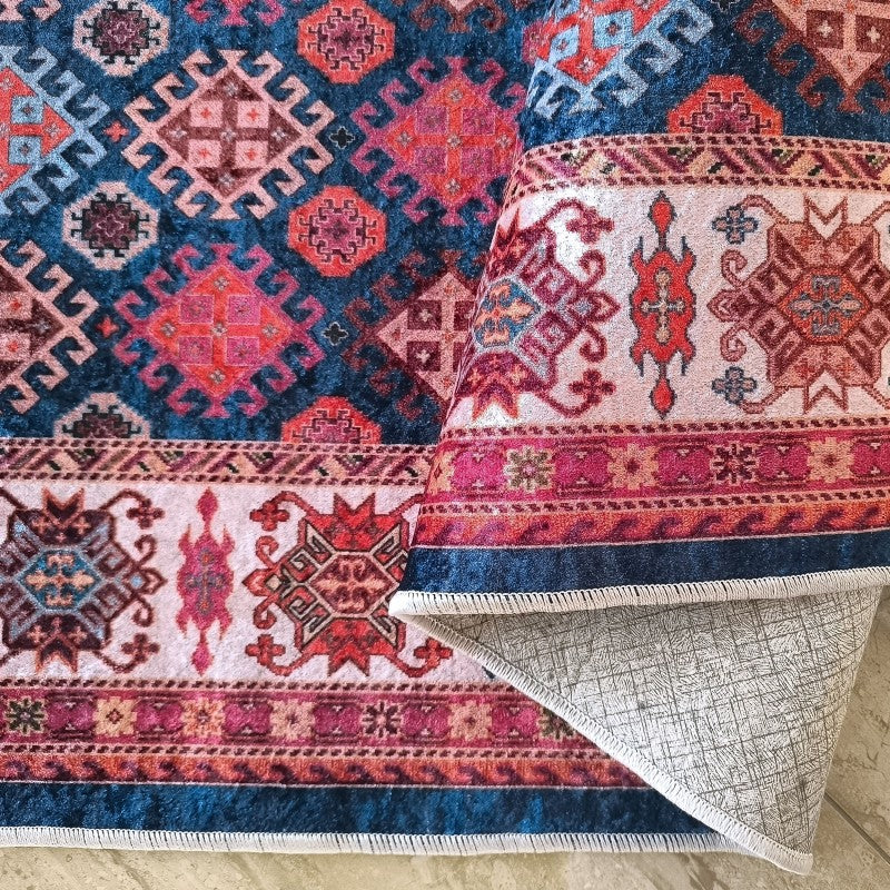 Tapis doux aux motifs géométriques traditionnels en rouge, rose, bleu et crème sur fond bleu foncé, partiellement plié