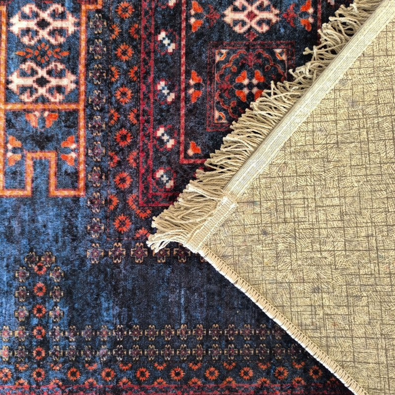 Tapis aux motifs traditionnels rouges et bleus avec franges, dont le coin relevé dévoile un envers beige quadrillé