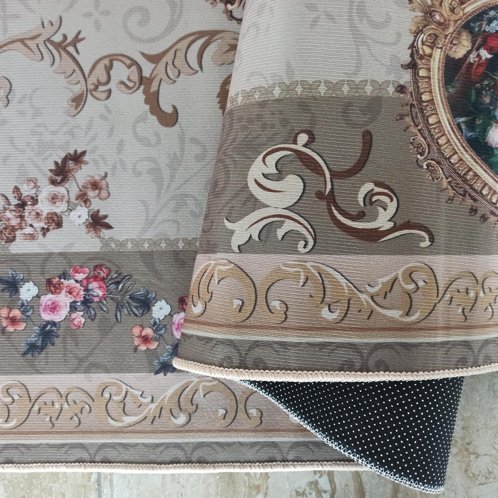 Tapis à motifs floraux roses, arabesques beiges et marron, et un grand médaillon doré. Son envers est noir à pois blancs