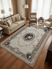 Tapis rectangulaire beige clair orné de motifs floraux classiques et de volutes marron, avec une bordure taupe, dans un salon