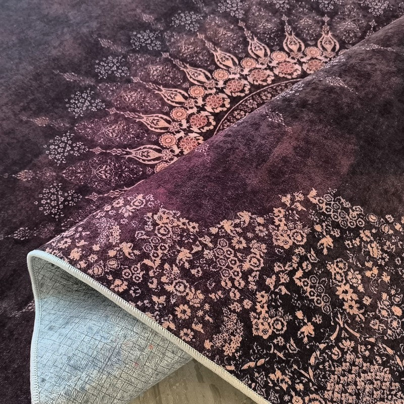 Tapis doux en tissu foncé, aux motifs floraux complexes rose clair. Une partie du tapis est repliée, révélant son envers