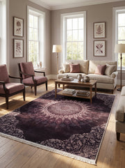 Grand tapis rectangulaire prune foncée à franges, avec un médaillon central et des motifs floraux rose poudré, dans un salon