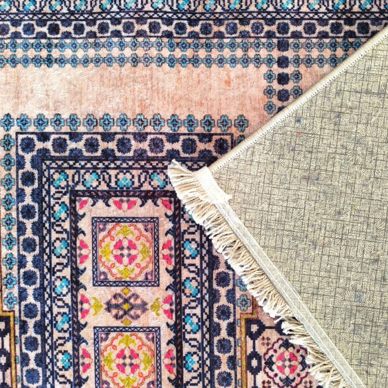 Tapis aux motifs floraux et géométriques colorés sur fond pêche. L'envers gris quadrillé et des franges sont visibles