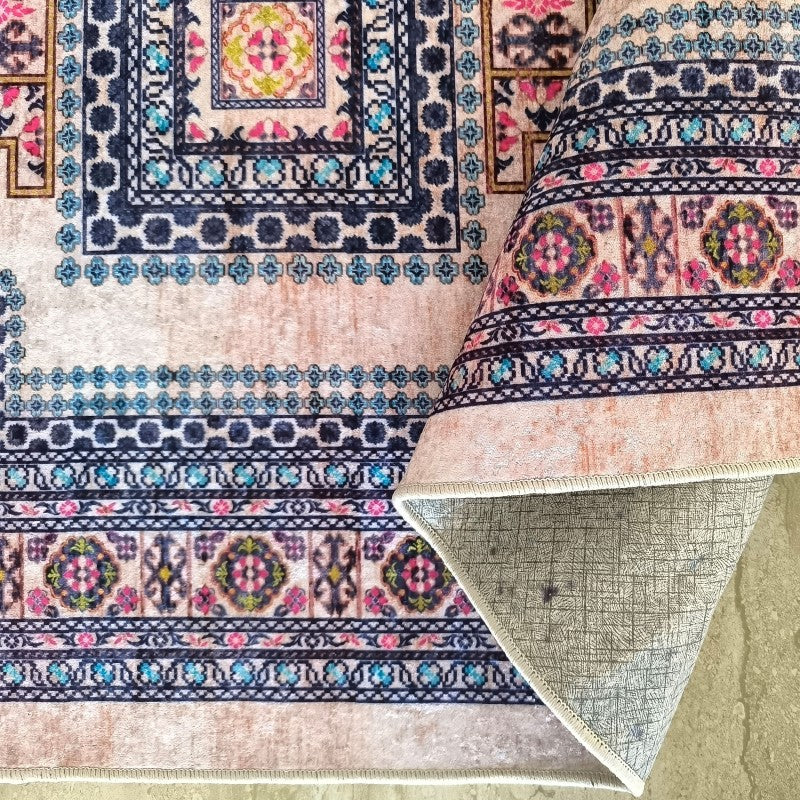 Tapis à motifs orientaux colorés en bleu, rose, jaune et vert sur fond beige rosé. Une partie est roulée, révélant l'envers gris texturé