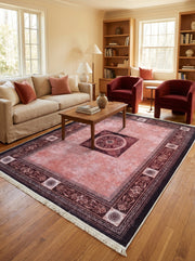 Grand tapis rectangulaire rose saumoné vieilli, bordures et médaillon central bordeaux avec motifs floraux classiques, dans un salon lumineux