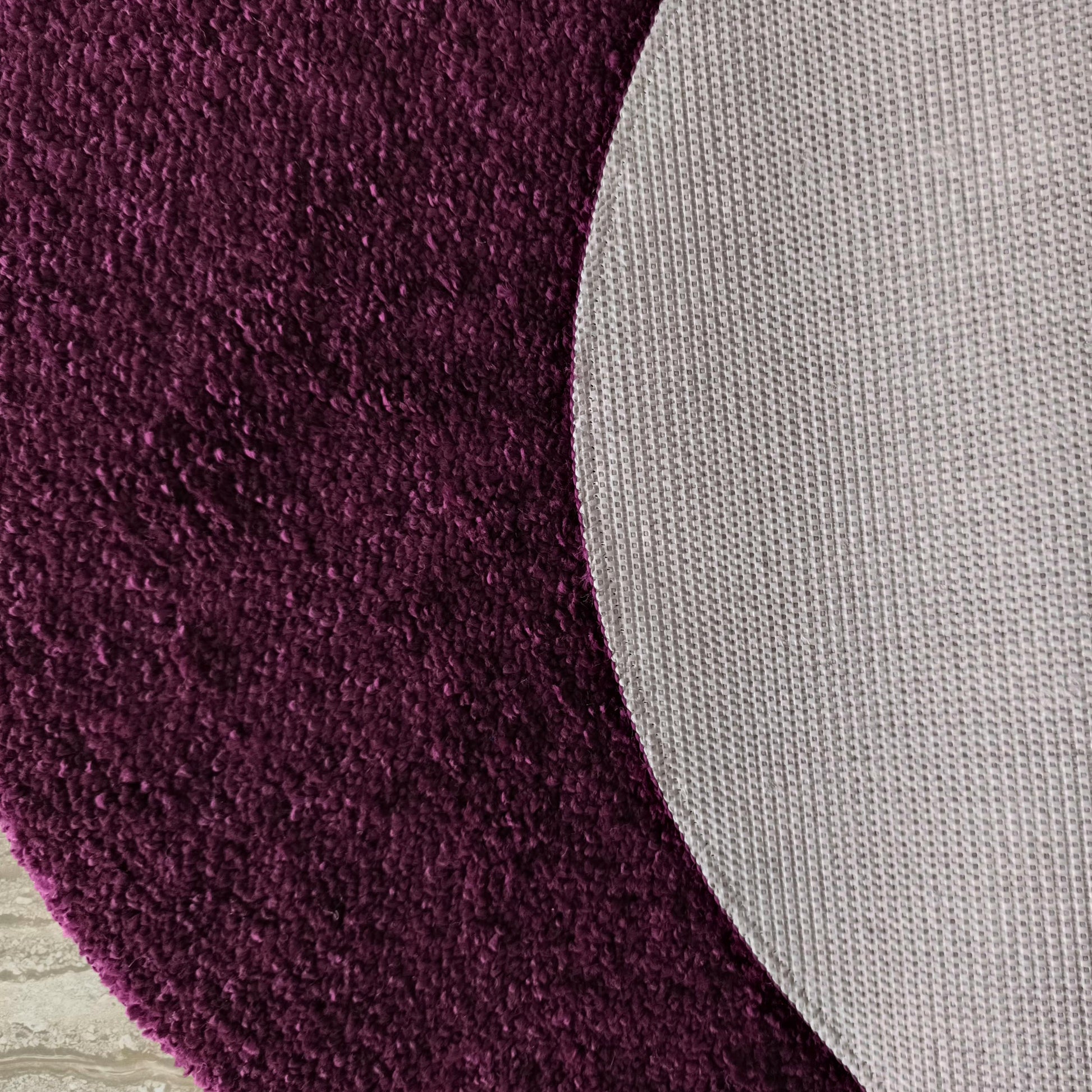 Tapis violet foncé à texture moelleuse, montrant son envers gris clair antidérapant avec un motif quadrillé