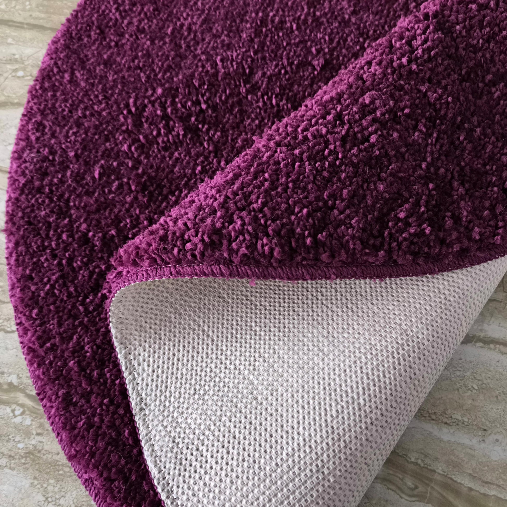 Tapis magenta profond à poils bouclés, une partie est retournée montrant son envers antidérapant gris sur un sol marbré