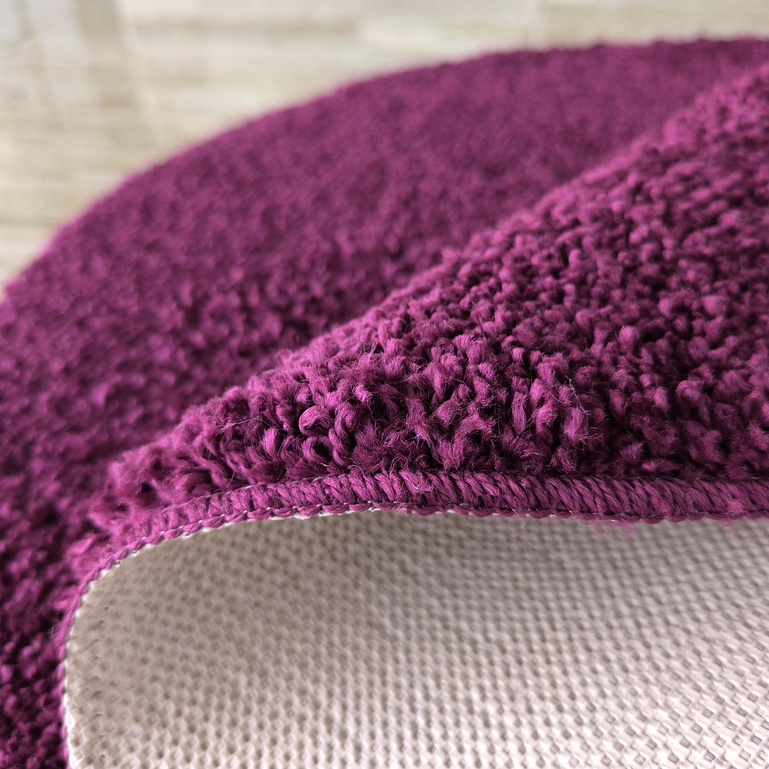 Gros plan sur un tapis violet foncé et moelleux, dont le bord est relevé, révélant le dessous texturé clair