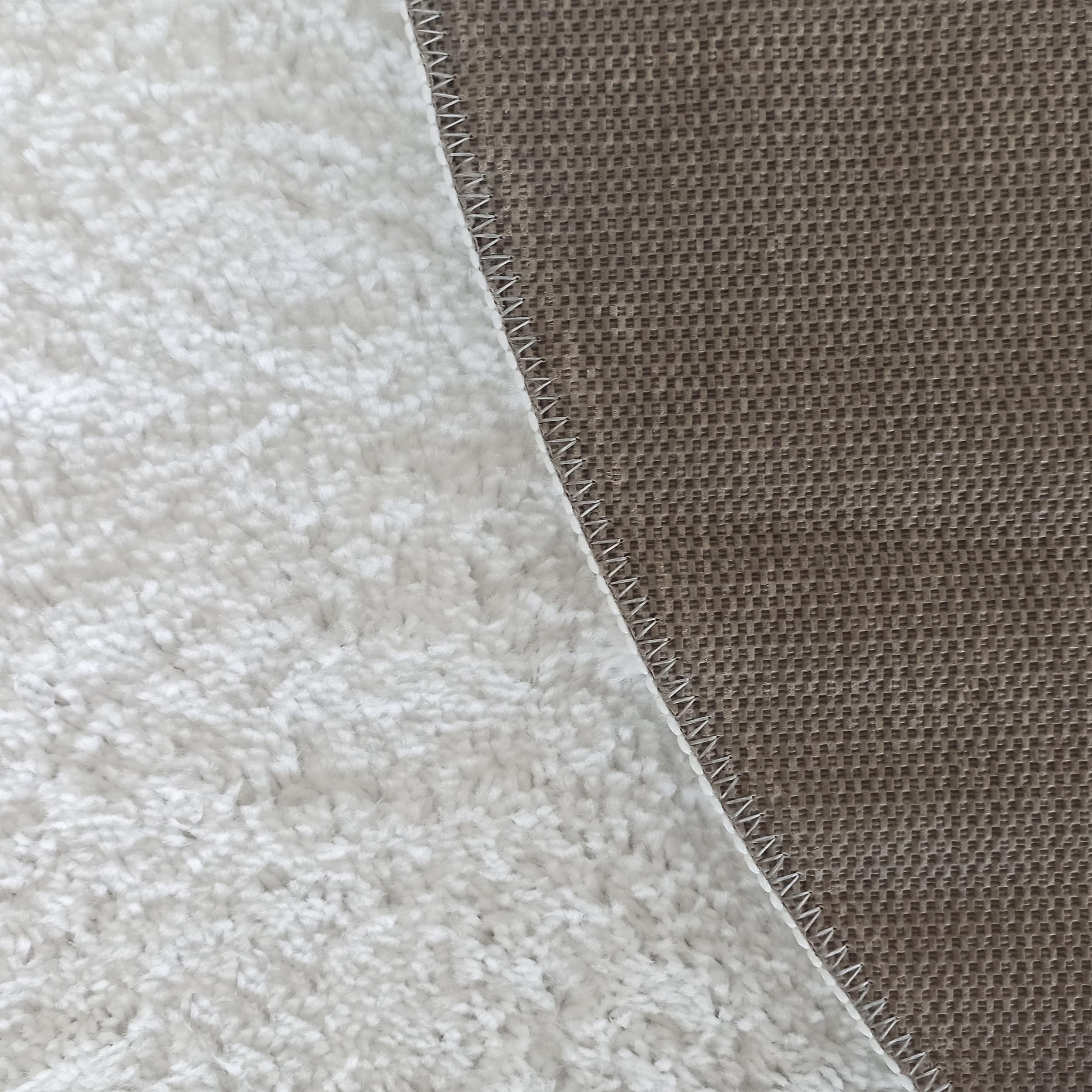 Tapis crème à poils longs et son envers texturé marron, avec une couture blanche sur le bord