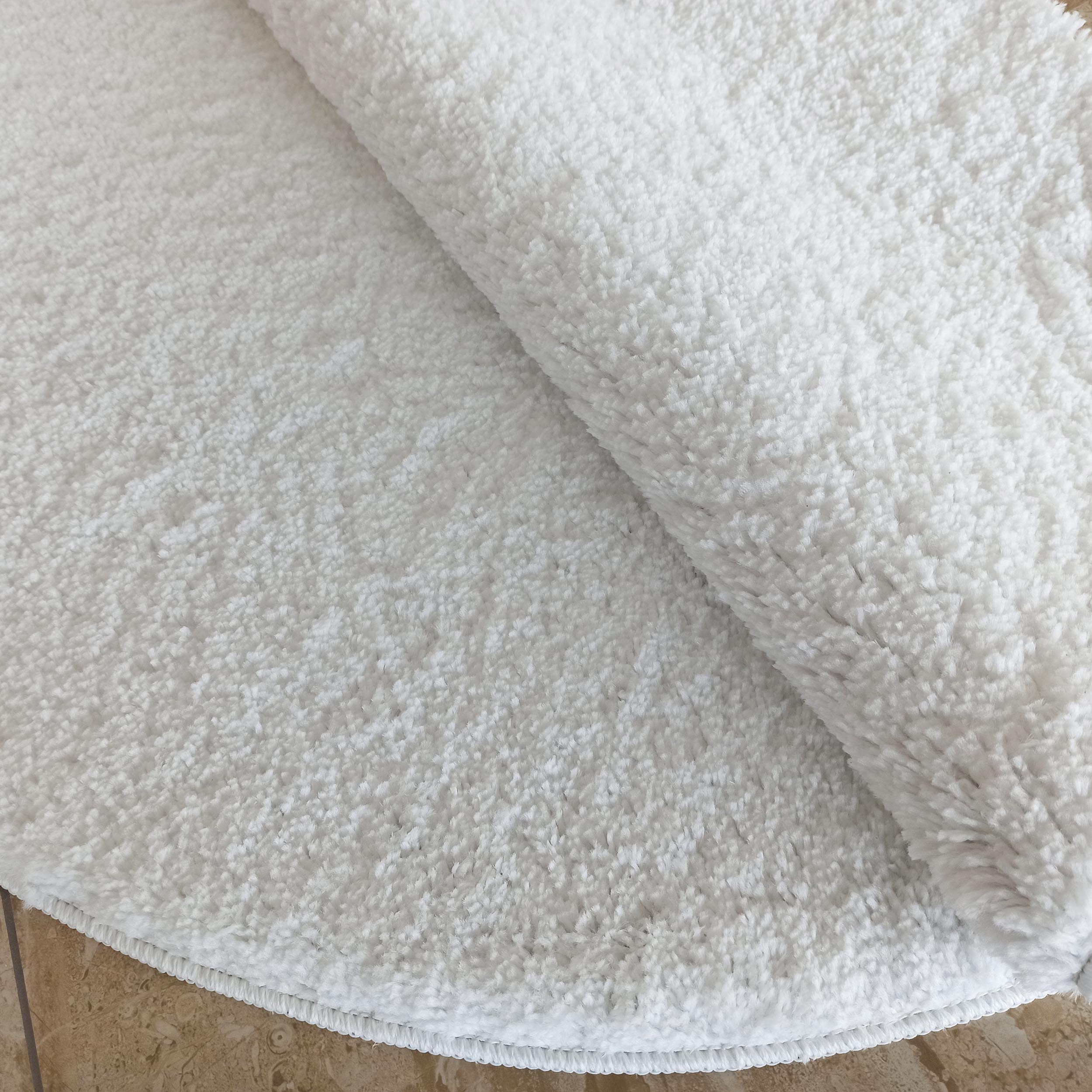 Tapis blanc doux et moelleux avec une texture shaggy, légèrement plié, montrant sa surface épaisse
