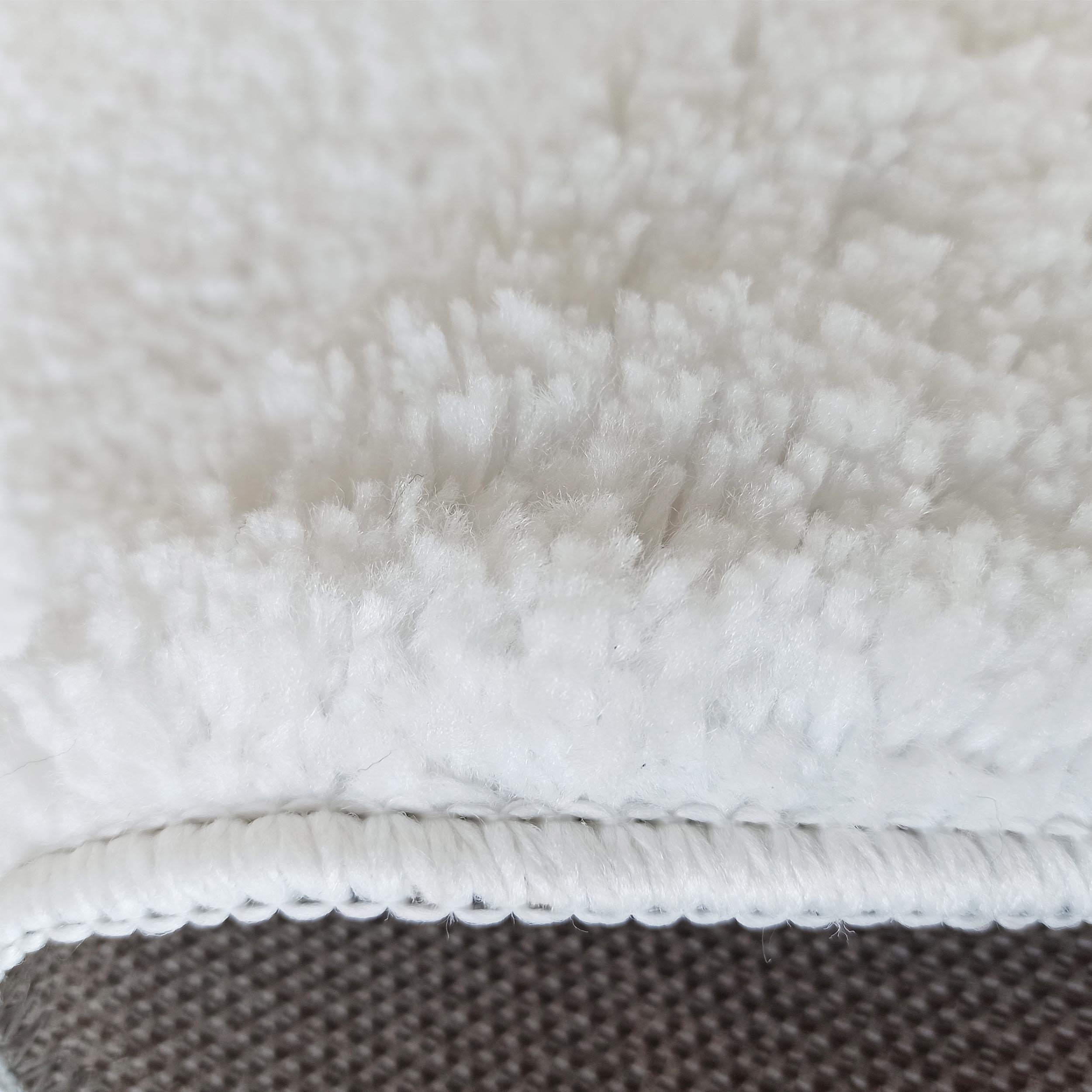 Gros plan d'un tapis blanc à poils longs et moelleux, avec une bordure blanche tressée et un dessous gris texturé