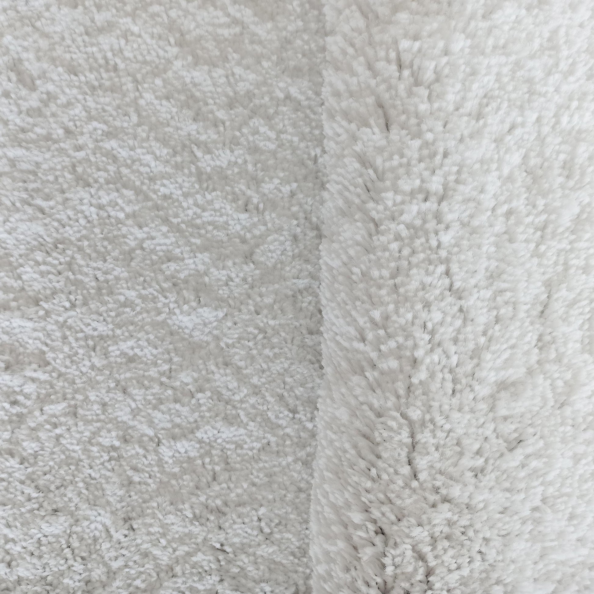 Tapis blanc cassé ou crème à texture douce et duveteuse, avec un côté à poils plus longs et épais
