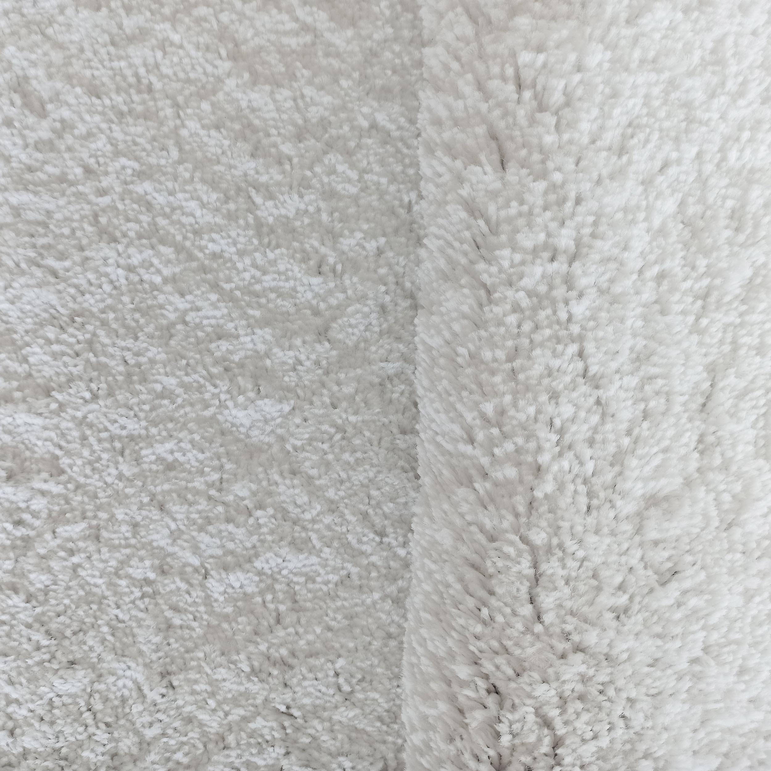 Tapis blanc cassé ou crème à texture douce et duveteuse, avec un côté à poils plus longs et épais