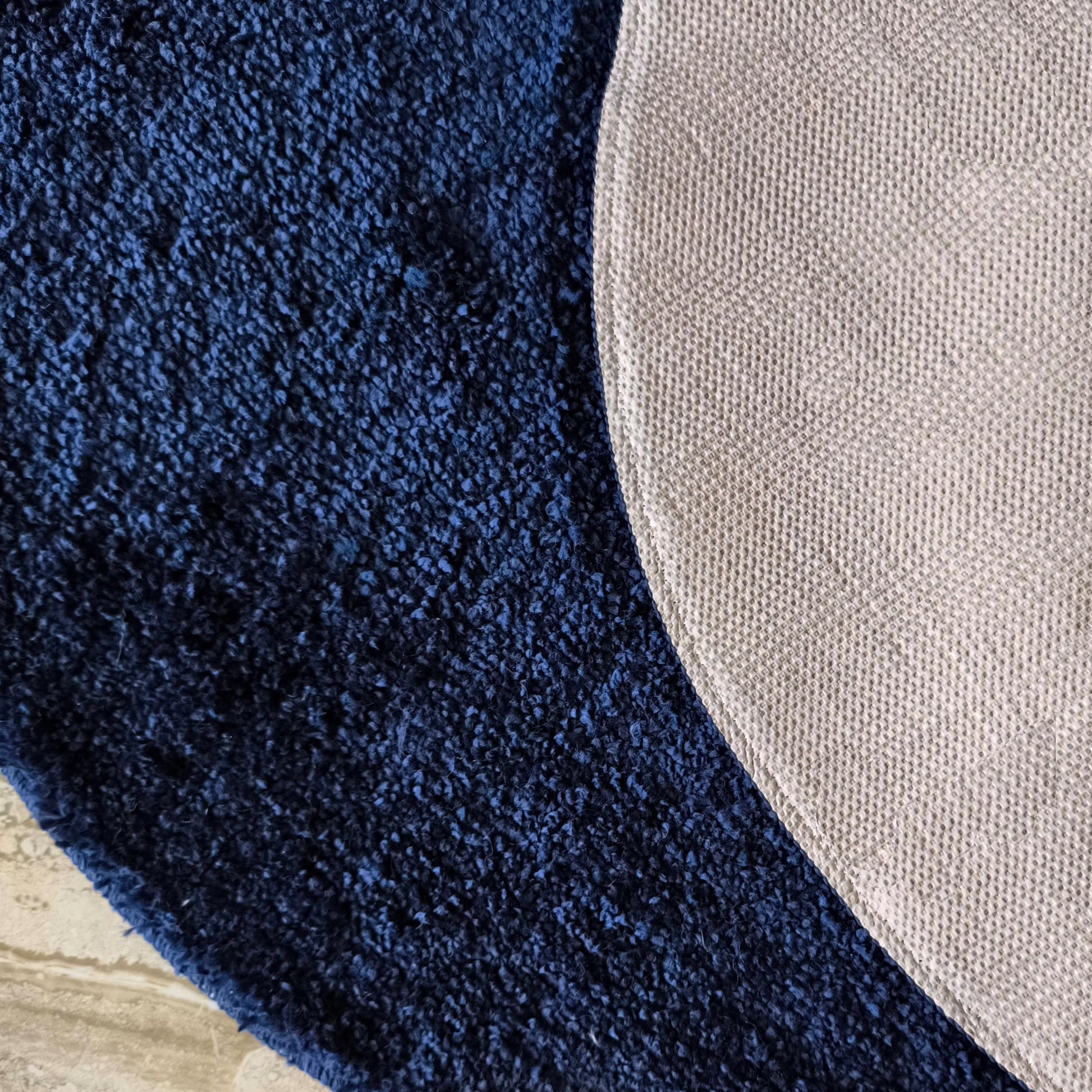 Tapis bleu foncé à longs poils, avec son envers beige clair structuré de petits motifs en relief