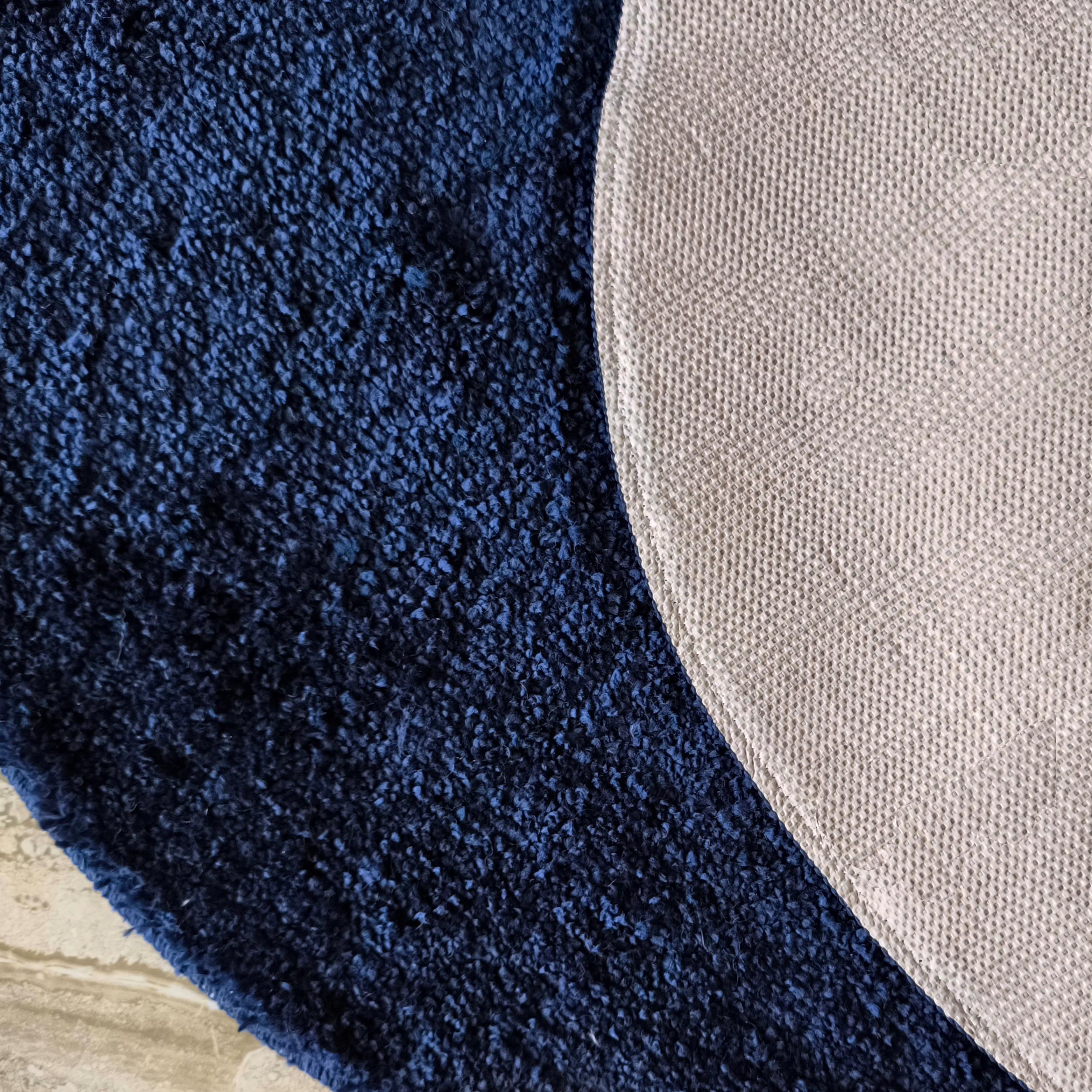 Tapis bleu foncé à longs poils, avec son envers beige clair structuré de petits motifs en relief