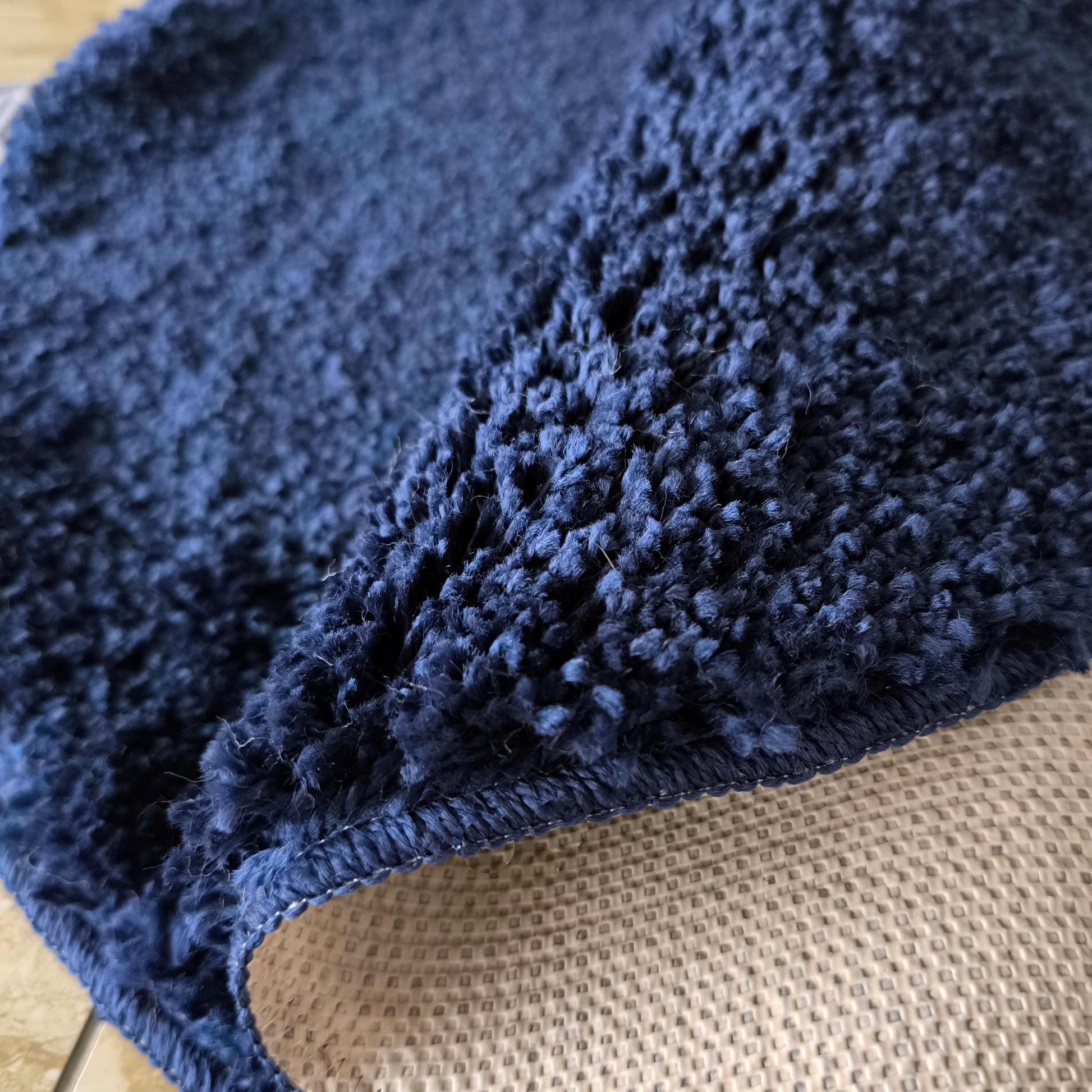 Un tapis bleu foncé à la texture moelleuse est relevé, dévoilant son envers beige au motif quadrillé
