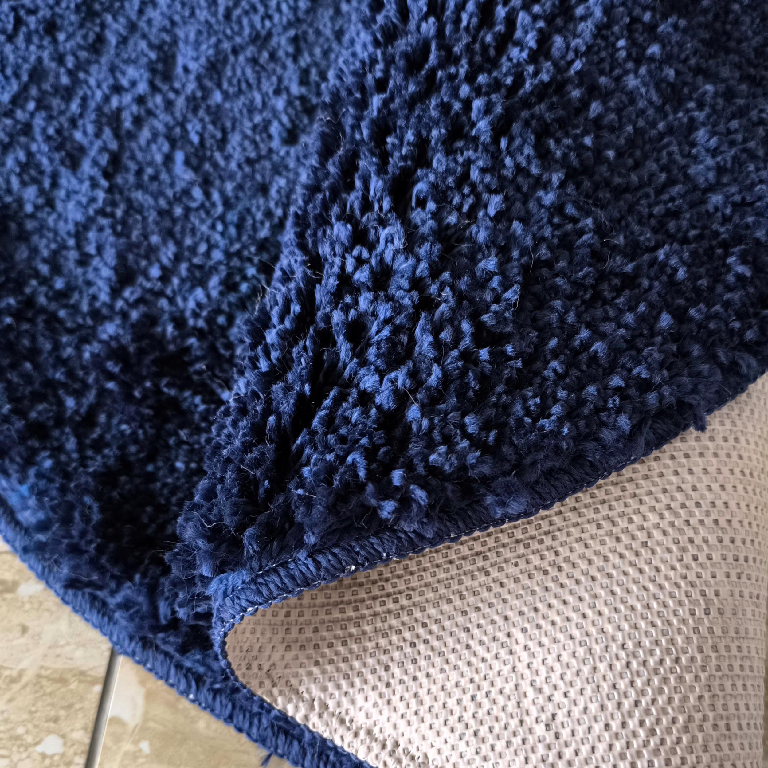 Tapis shaggy bleu marine partiellement enroulé montrant son envers antidérapant beige clair texturé