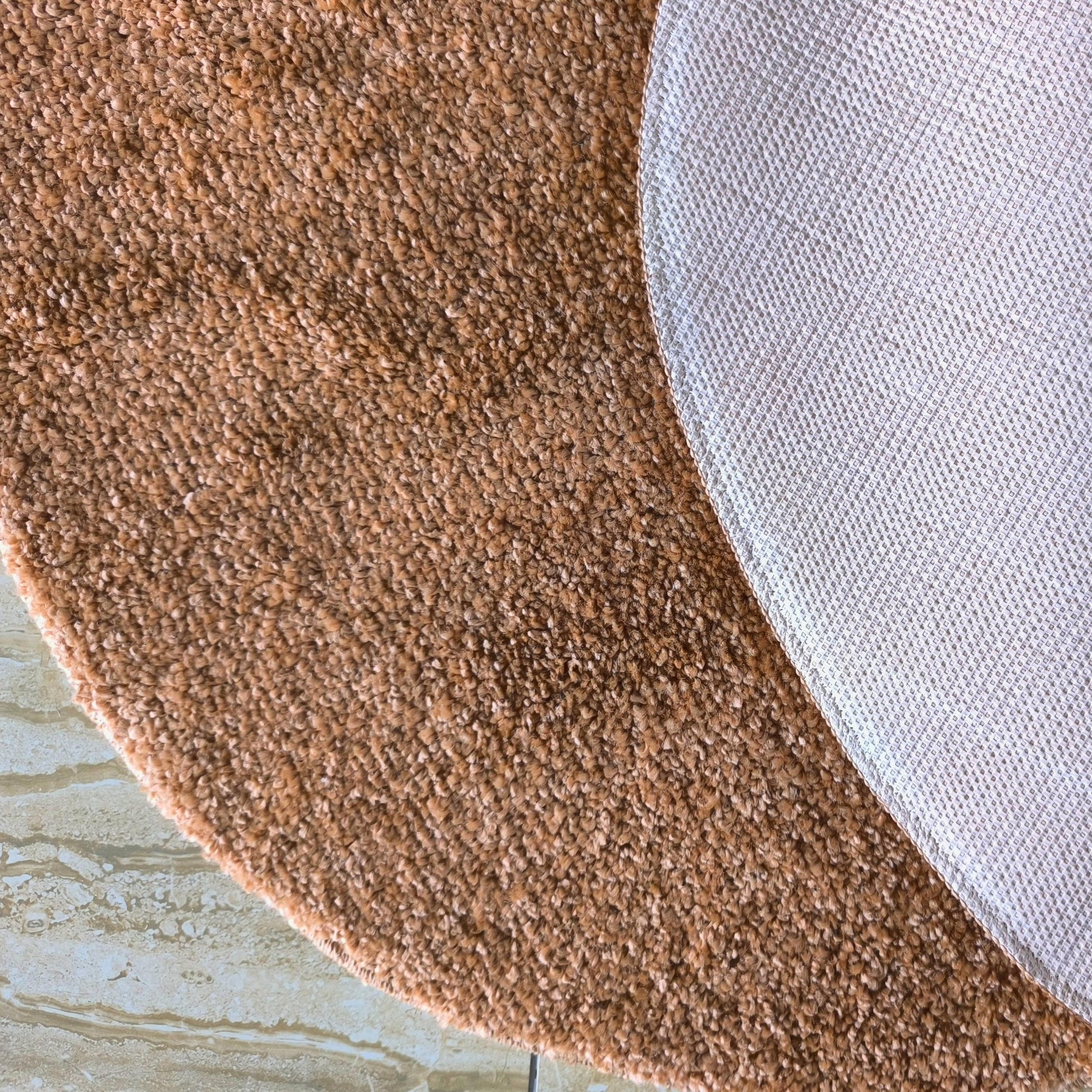Tapis moelleux aux tons marron clair et beige sur sol carrelé, révélant son envers antidérapant blanc quadrillé
