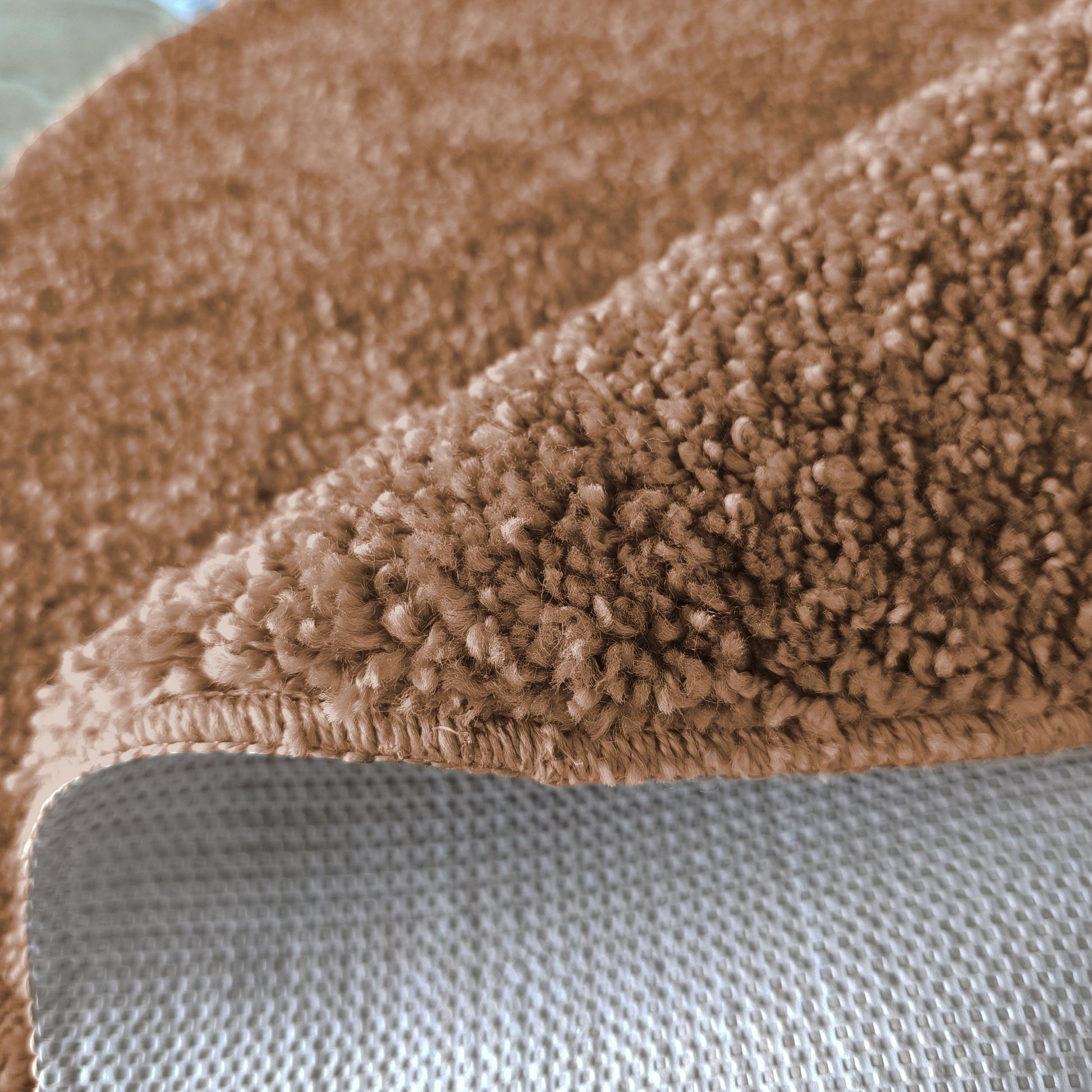 Tapis doux et épais marron clair, avec des boucles de poils visibles. Un bord est replié sur son dessous à motif quadrillé gris