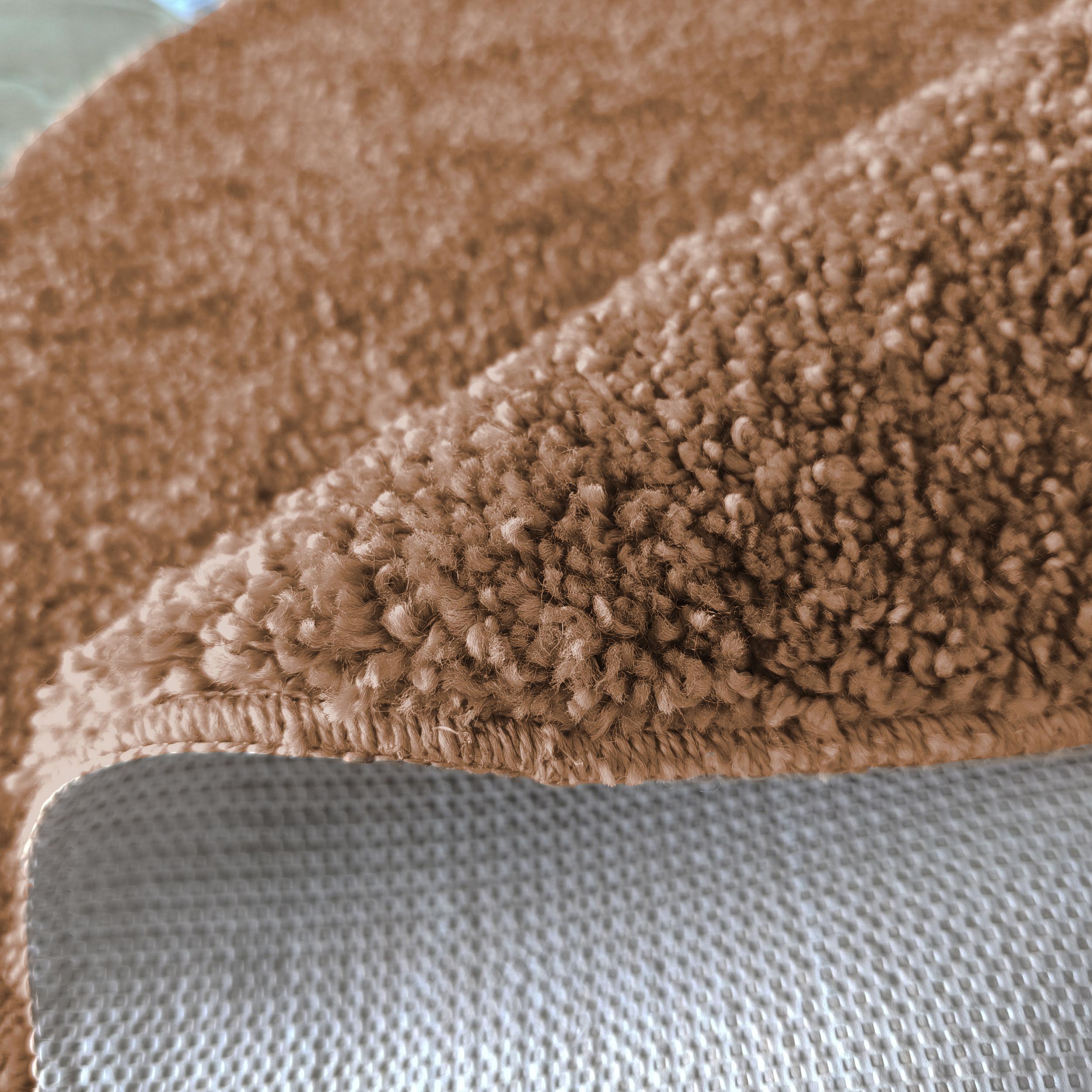 Tapis doux et épais marron clair, avec des boucles de poils visibles. Un bord est replié sur son dessous à motif quadrillé gris