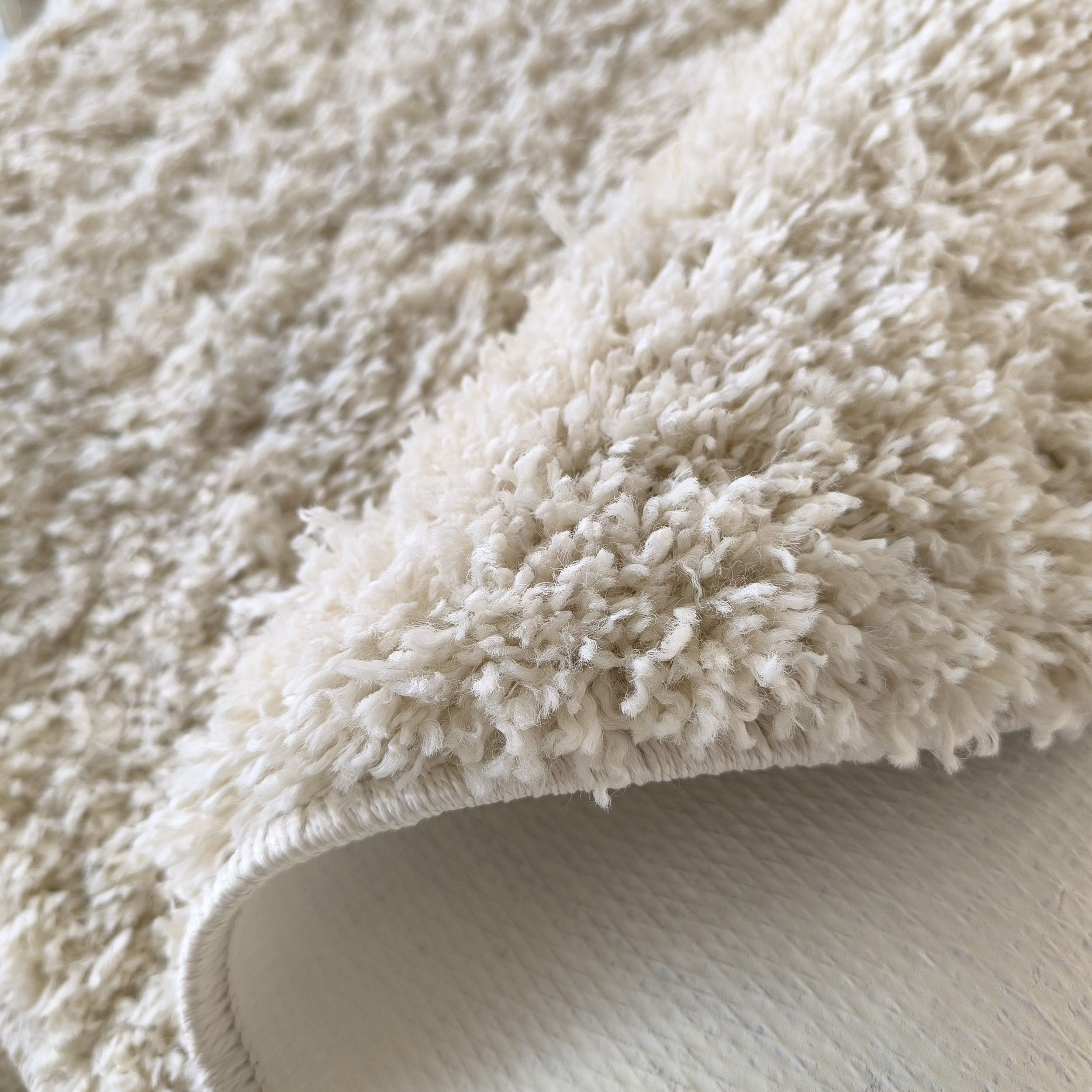 Gros plan d'un tapis crème à poils longs et doux, légèrement plié sur le côté
