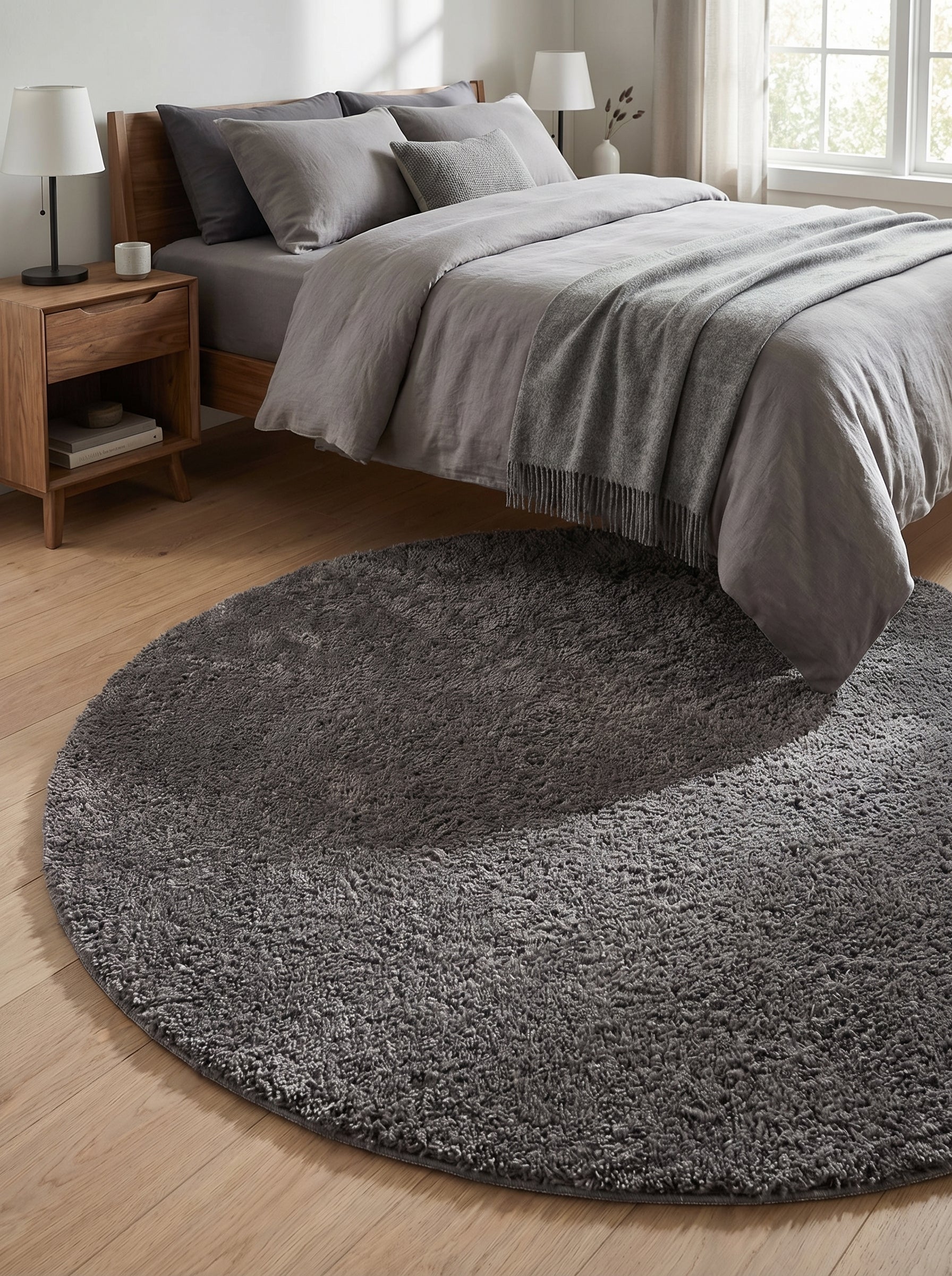 Tapis rond gris anthracite à poils longs et moelleux posé sur un parquet en bois clair devant un lit dans une chambre moderne