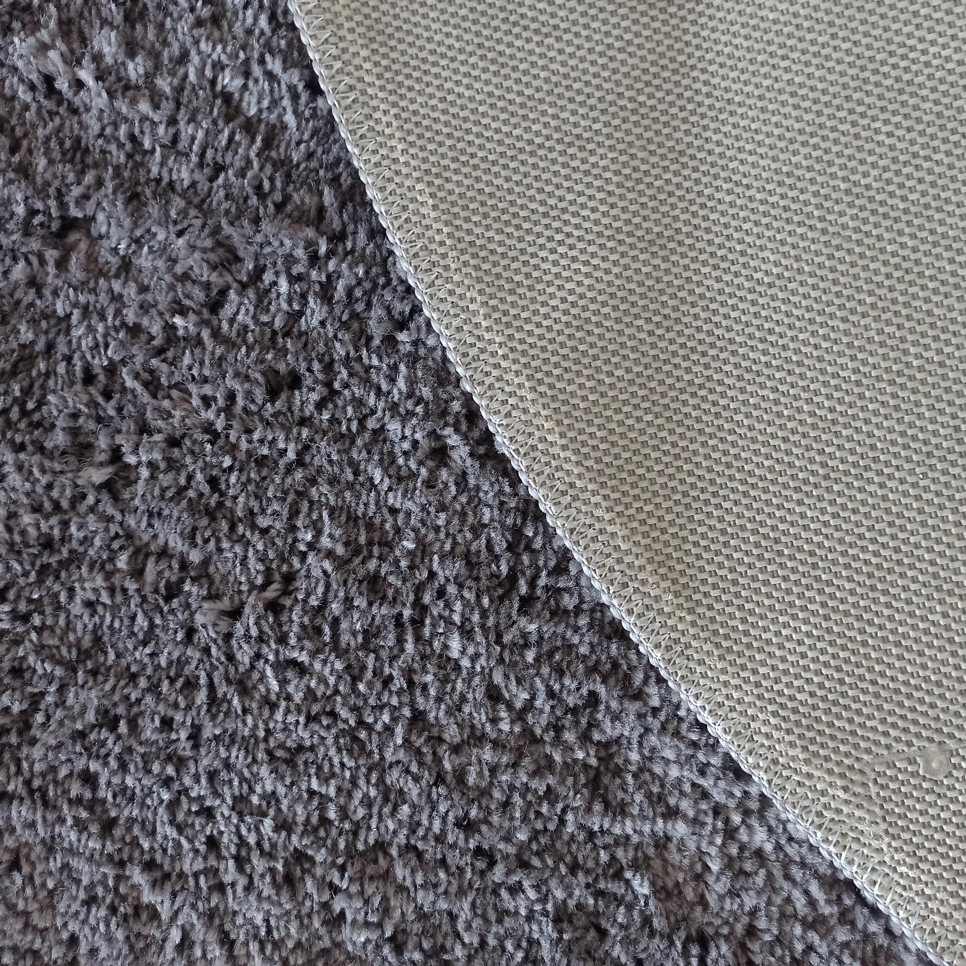 Tapis gris à longs poils duveteux, montrant son envers beige à motif tissé et une bordure cousue