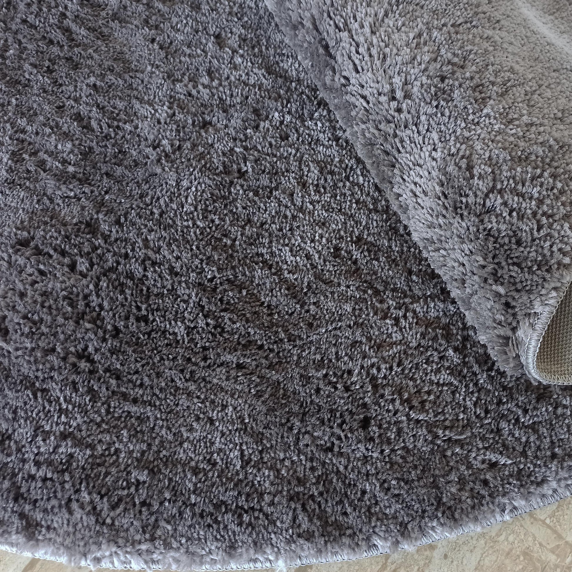 Tapis gris aux longs poils doux et nuancés, partiellement roulé, montrant son bord et sa texture dense