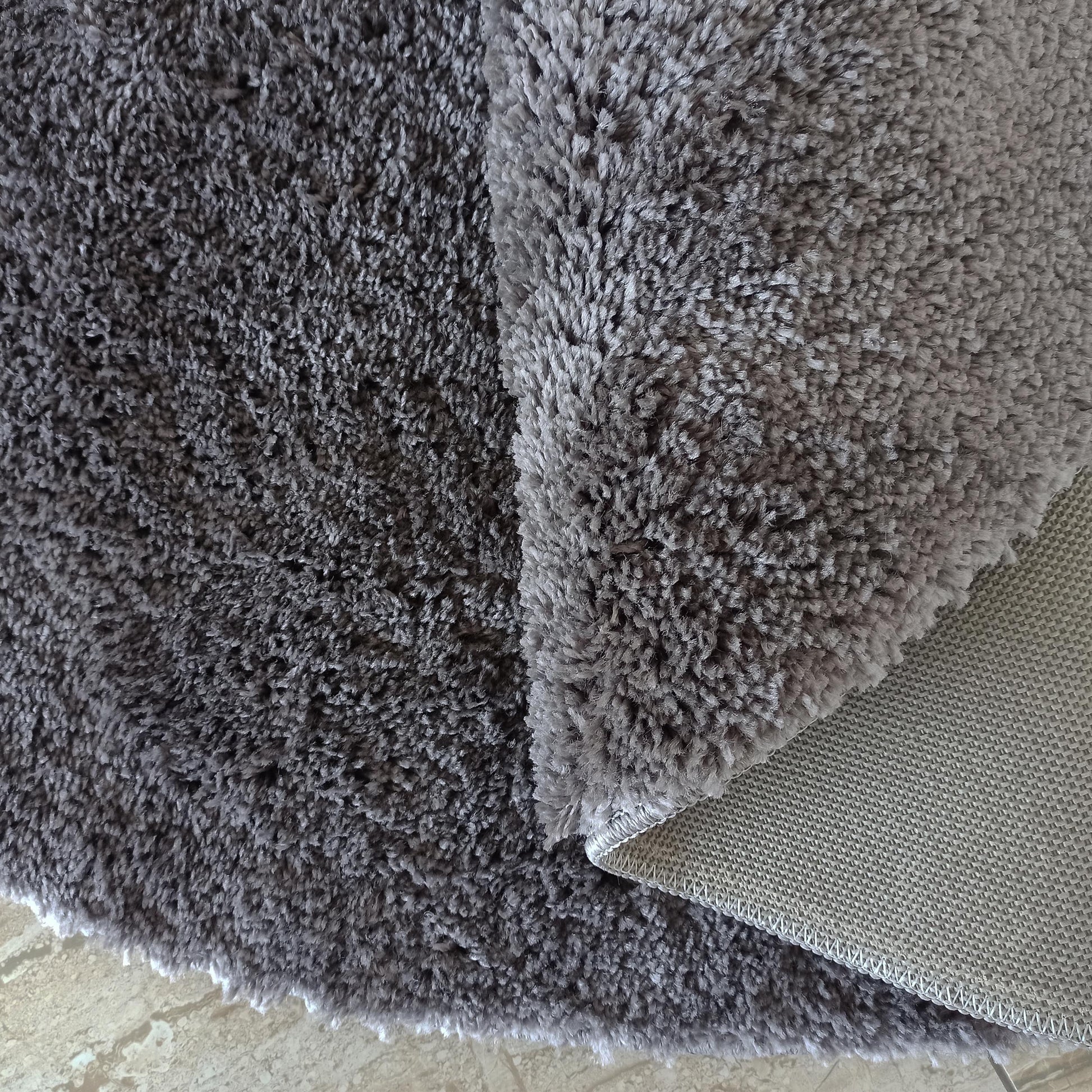 Tapis à poils longs gris anthracite, partiellement plié pour révéler une surface plus claire et un envers beige tissé