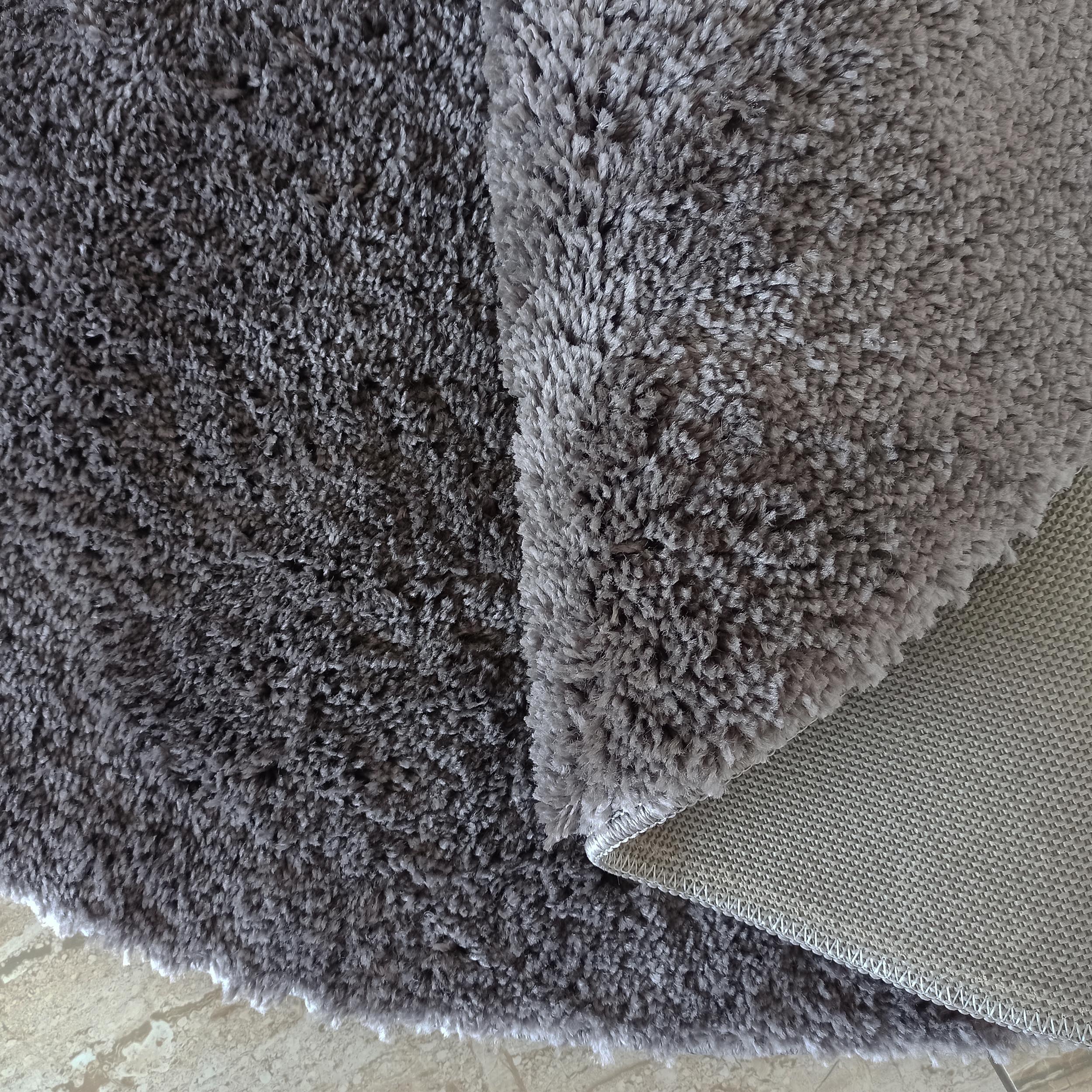 Tapis à poils longs gris anthracite, partiellement plié pour révéler une surface plus claire et un envers beige tissé