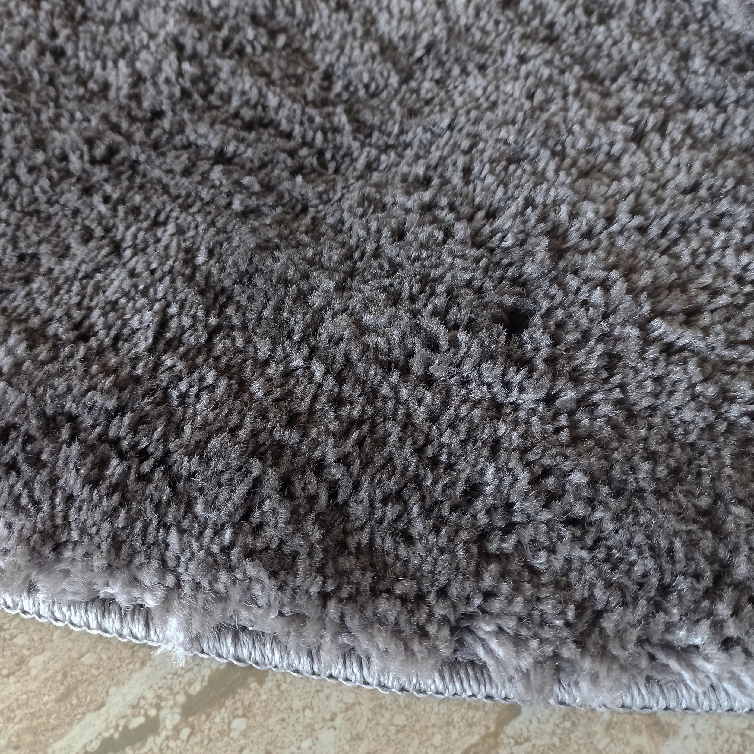 Tapis en textile à poils longs et épais de couleur gris nuancé, avec un bord surélevé visible sur un sol beige clair