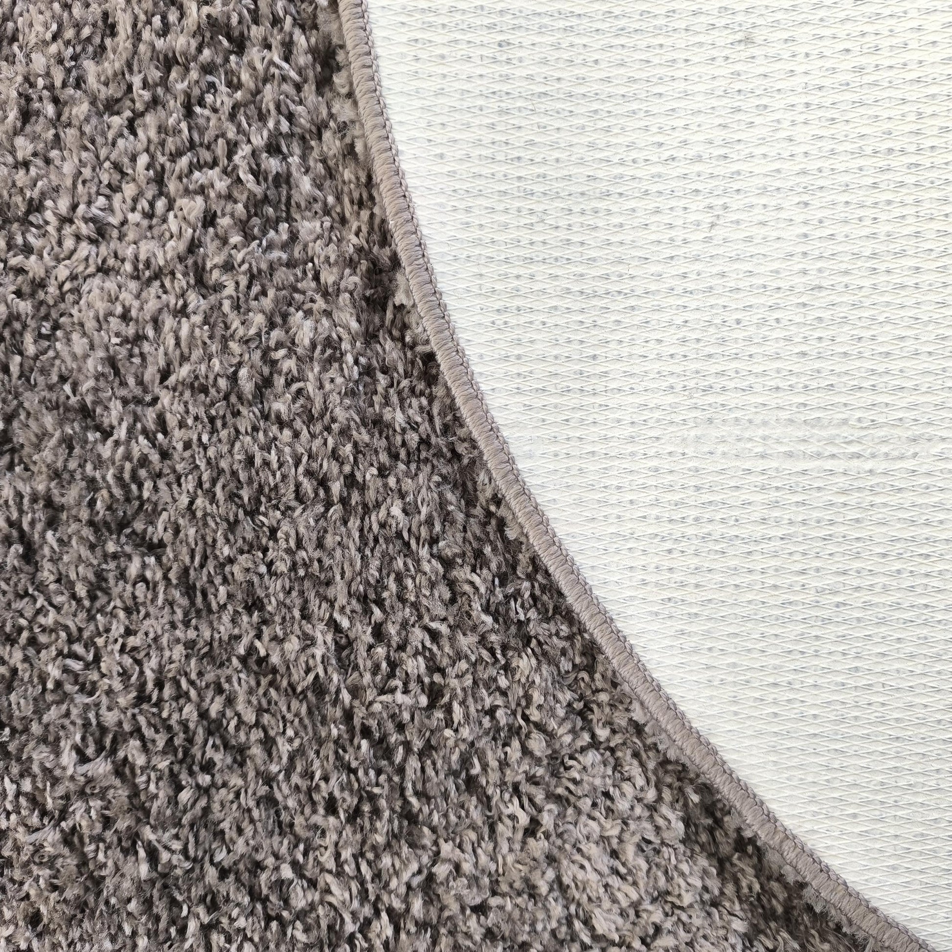 Tapis texturé gris et blanc, montrant le côté à poils longs et le dessous antidérapant à motif quadrillé