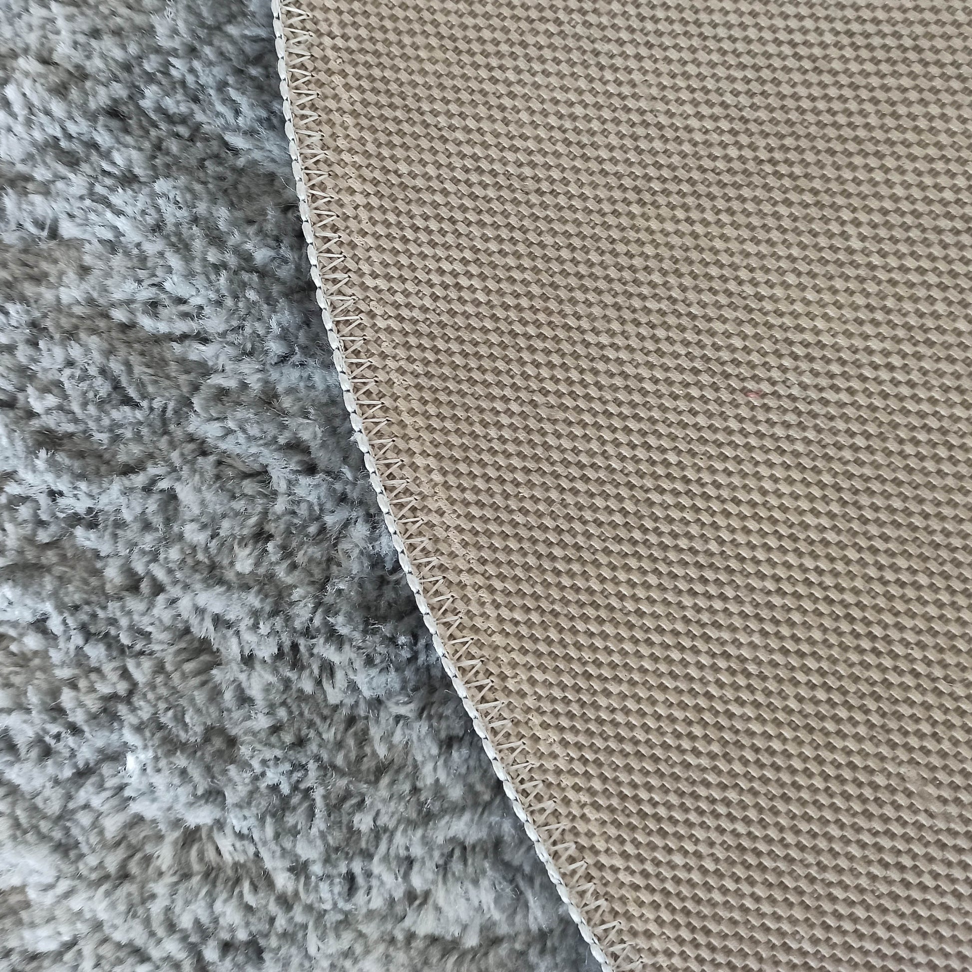 Un tapis présentant sa face supérieure grise et duveteuse à gauche, et son envers beige à motif tissé visible à droite, reliés par une couture blanche
