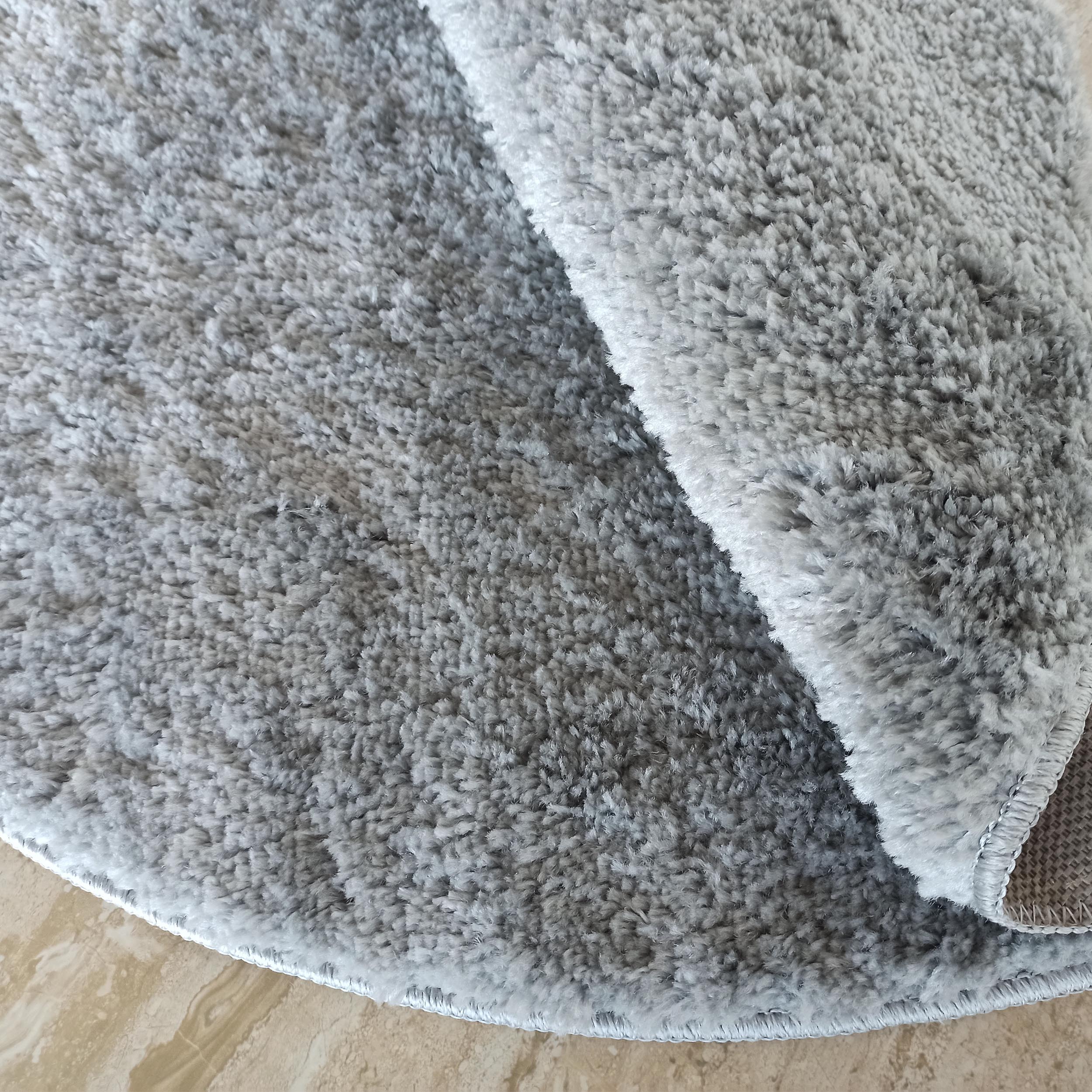 Tapis moelleux gris clair avec une texture à poils longs, partiellement enroulé sur un sol marbré beige
