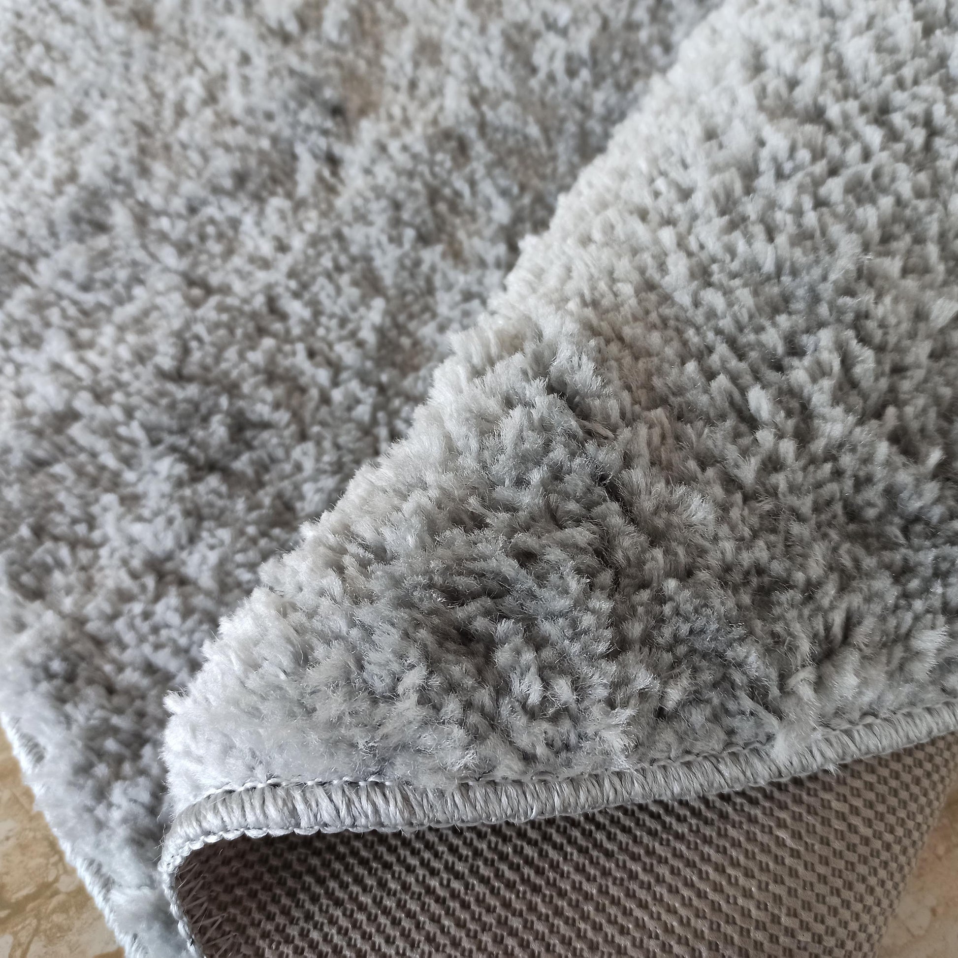 Tapis gris clair à poils longs et doux, plié pour révéler son envers tissé avec un motif géométrique