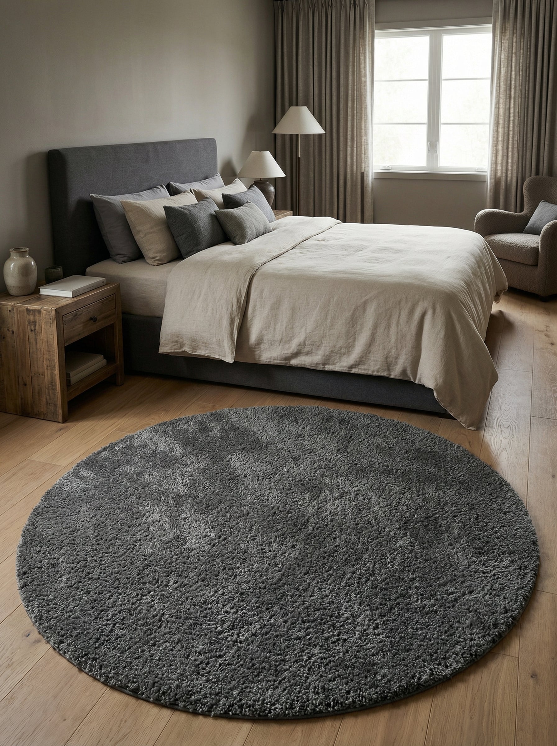 Tapis rond gris anthracite shaggy, à poils longs et doux, posé sur un parquet clair dans une chambre à coucher