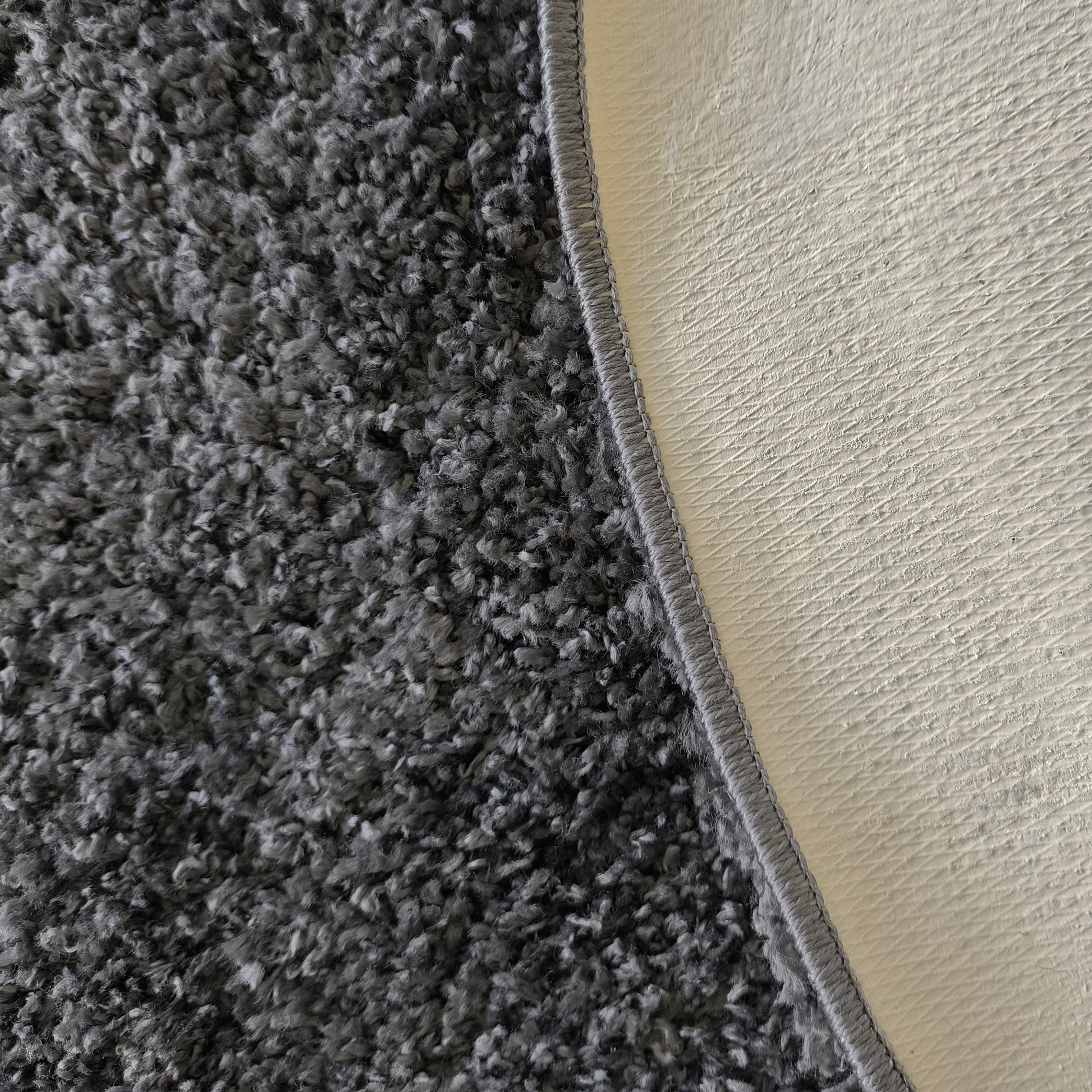 Tapis gris foncé à poils longs et texture shaggy, bordé de gris et montrant son revers clair texturé