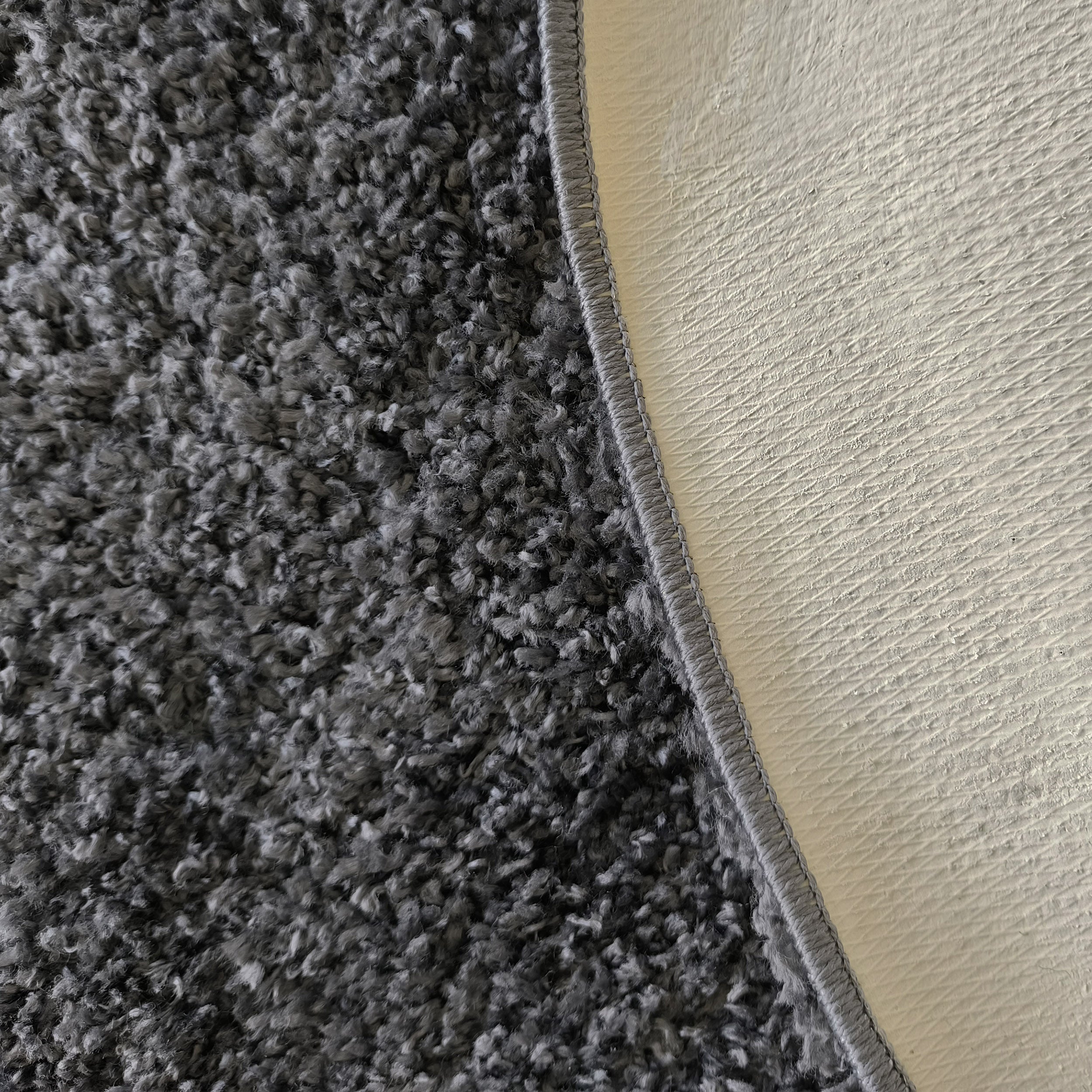 Tapis gris foncé à poils longs et texture shaggy, bordé de gris et montrant son revers clair texturé