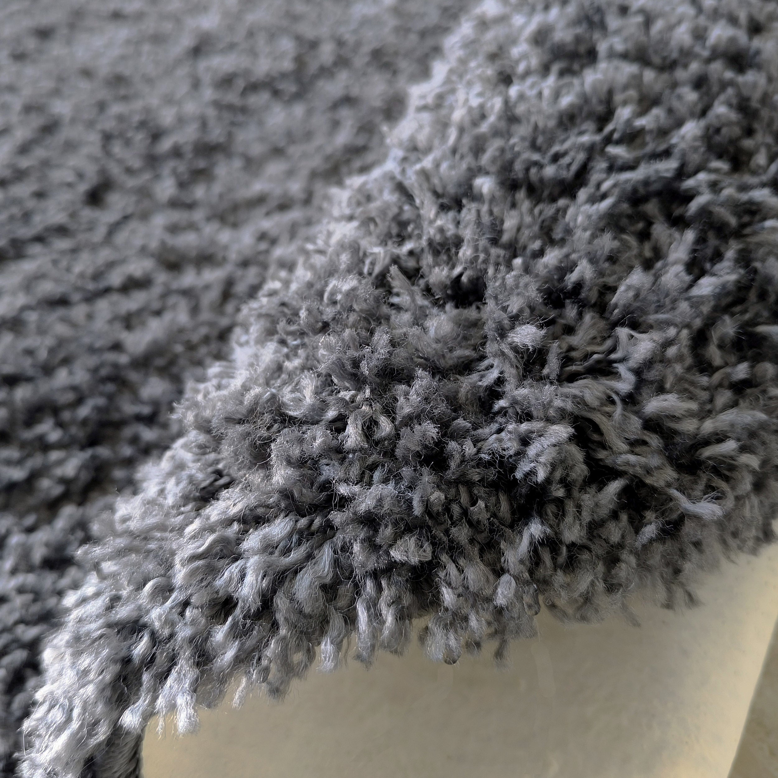 Gros plan sur un tapis épais à poils longs, aux nuances de gris, roulé en partie et montrant sa texture douce