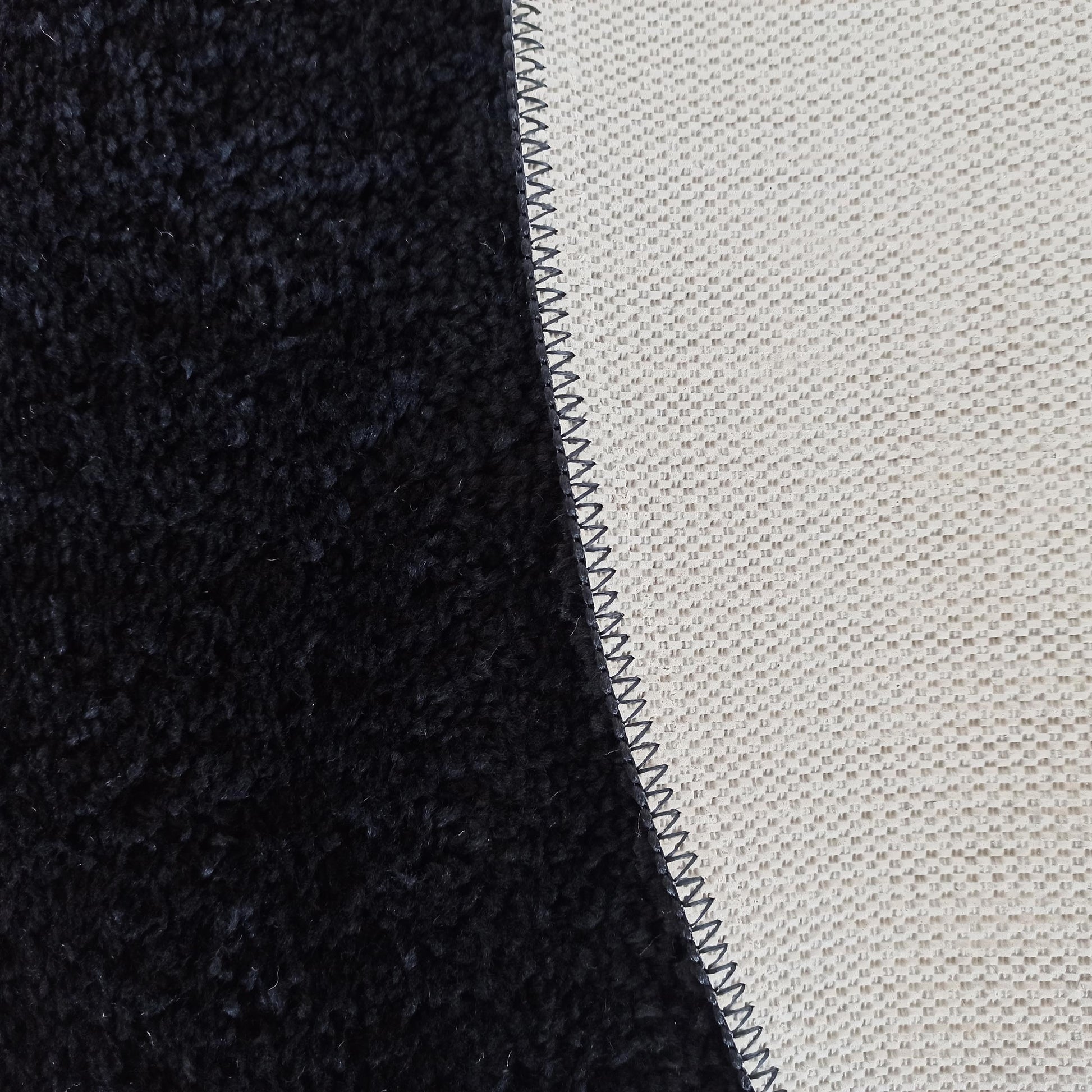 Détail d'un tapis présentant une texture à poils longs foncée et une surface tissée claire, reliées par une couture zigzag foncée